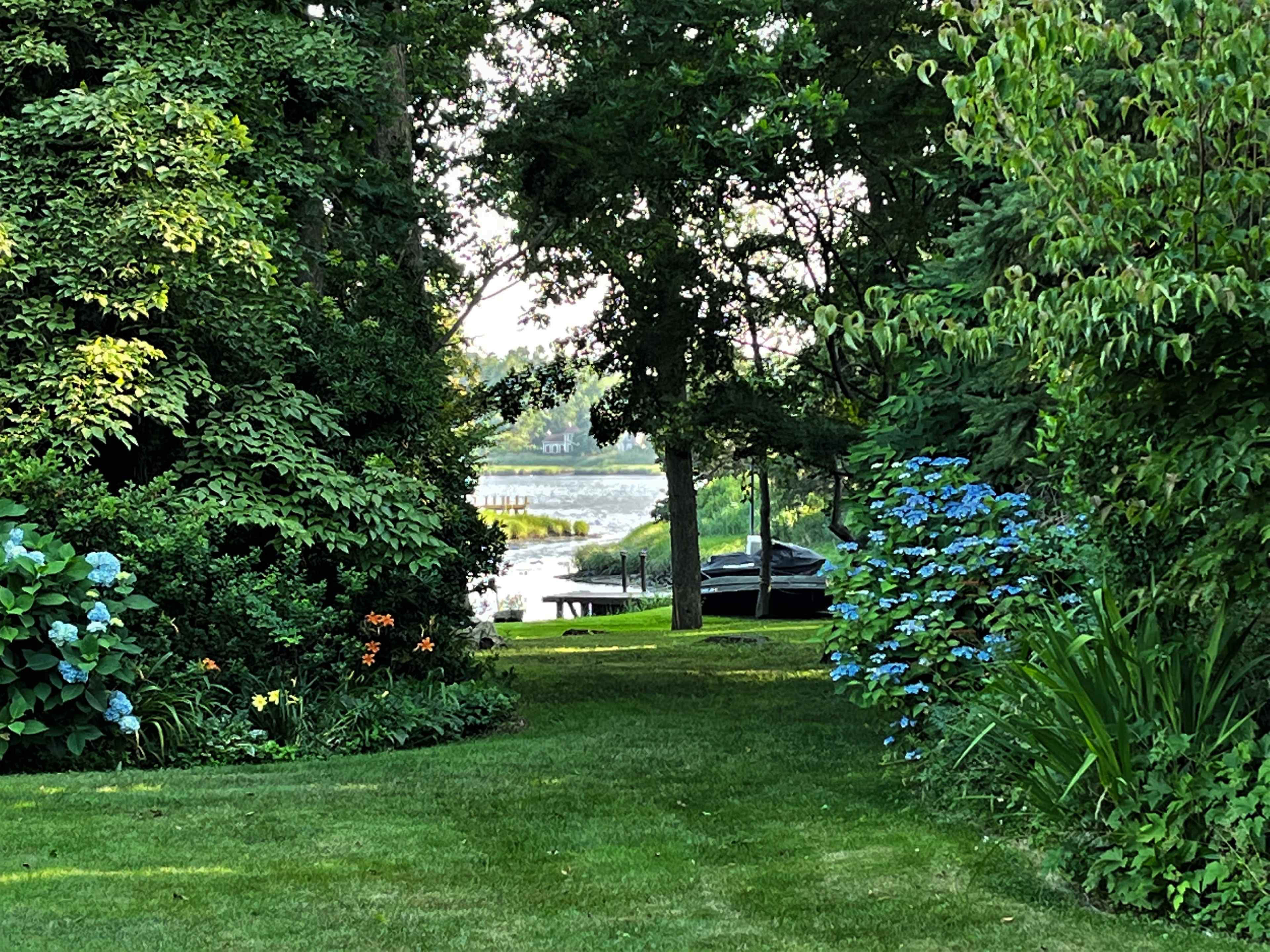 A path leads through lush greenery to a river with a docked boat in the background.