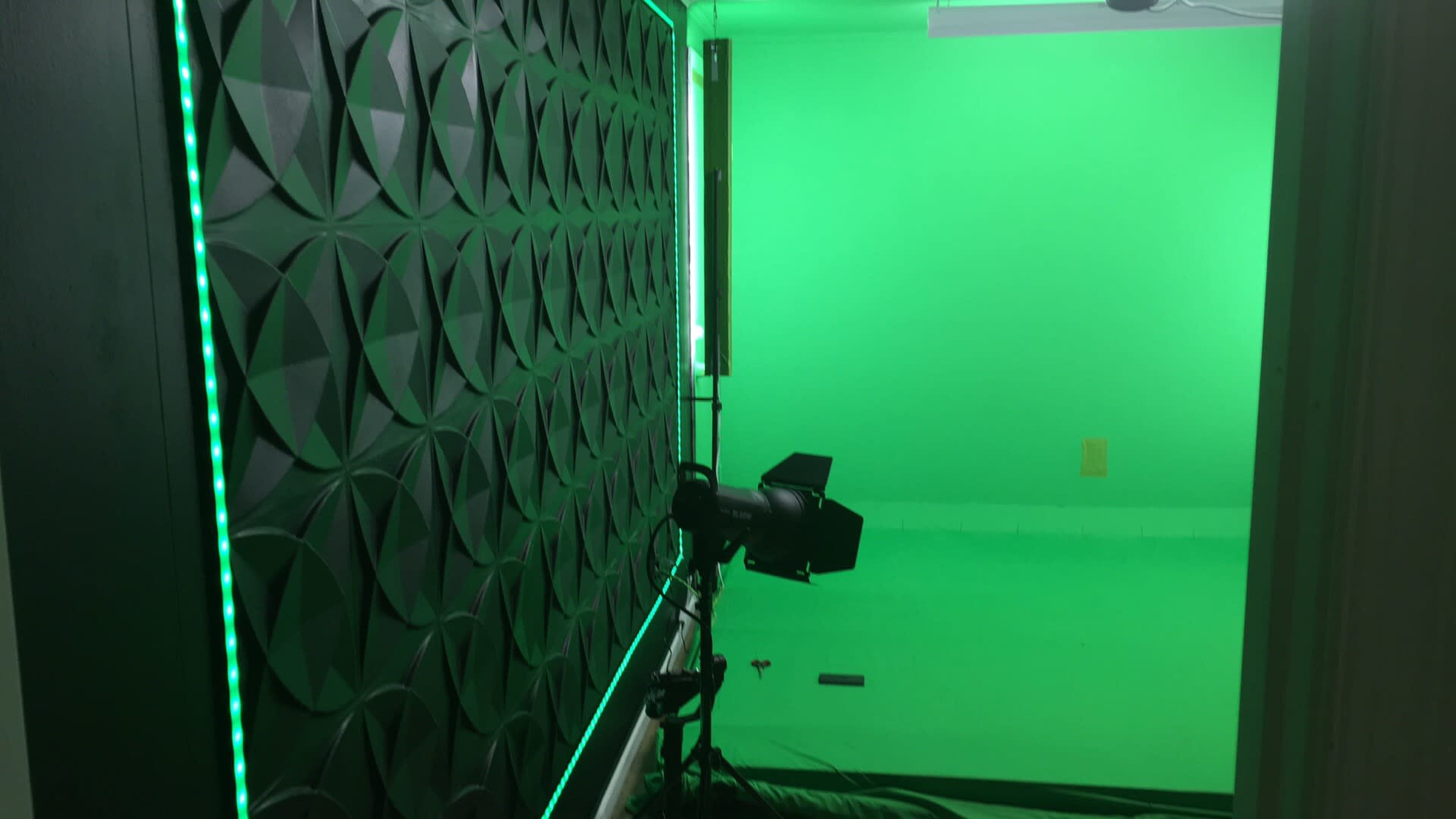 A green screen studio with a textured black wall and lighting equipment set up against a green background.