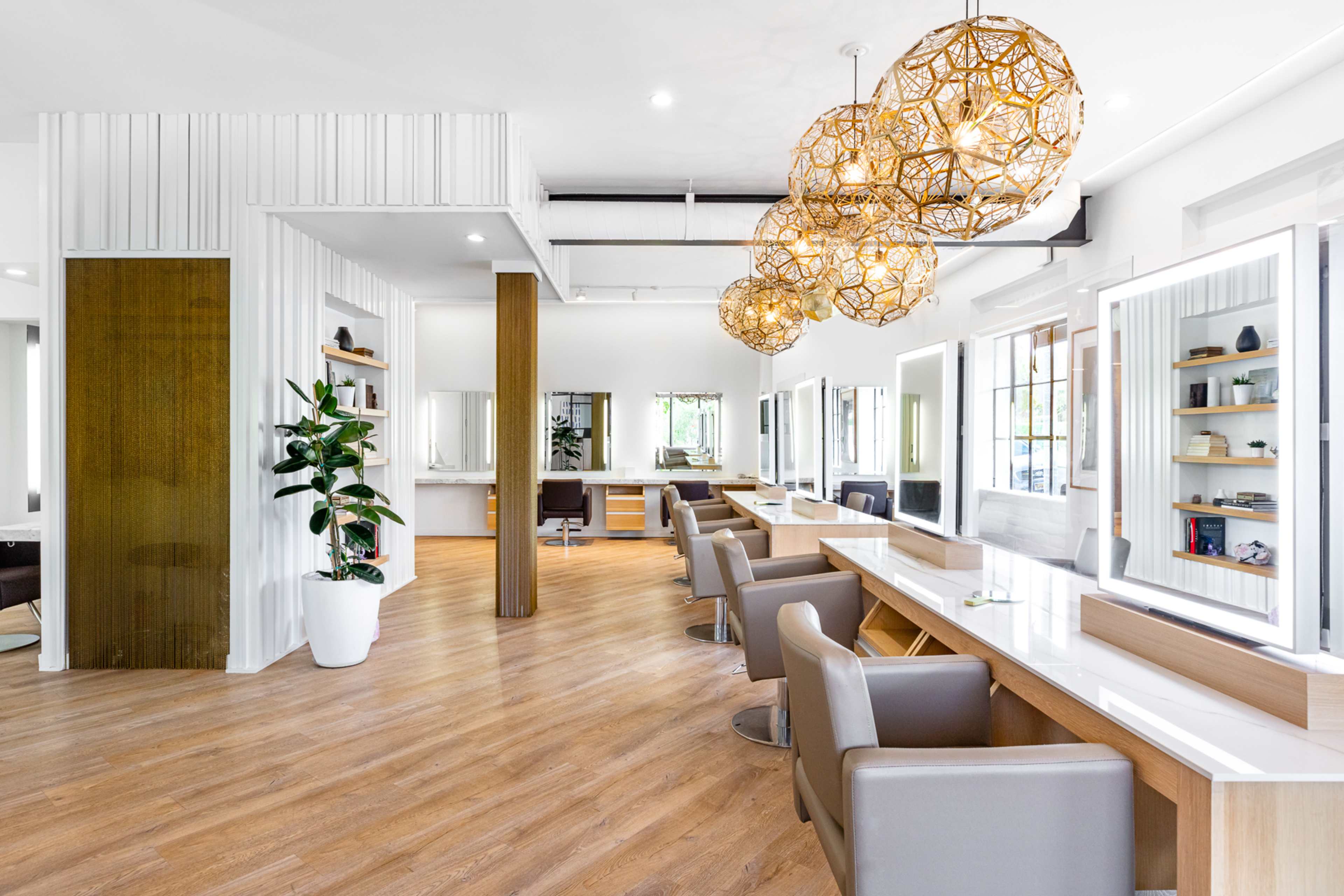A modern hair salon featuring multiple styling stations with large mirrors, comfortable chairs, and decorative pendant lighting.