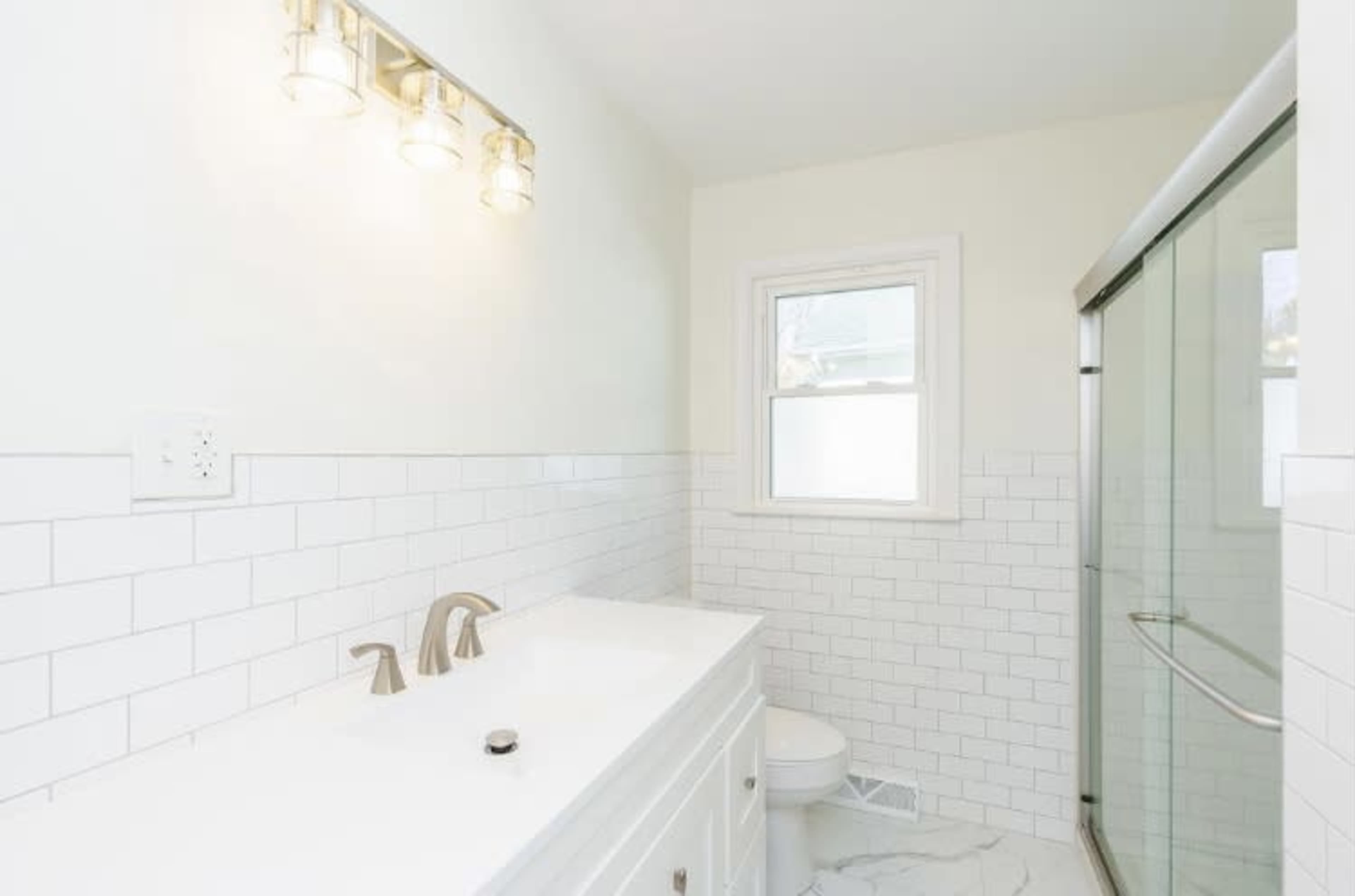 A clean bathroom with a double sink vanity, a shower with a glass door, and white subway tile on the walls.
