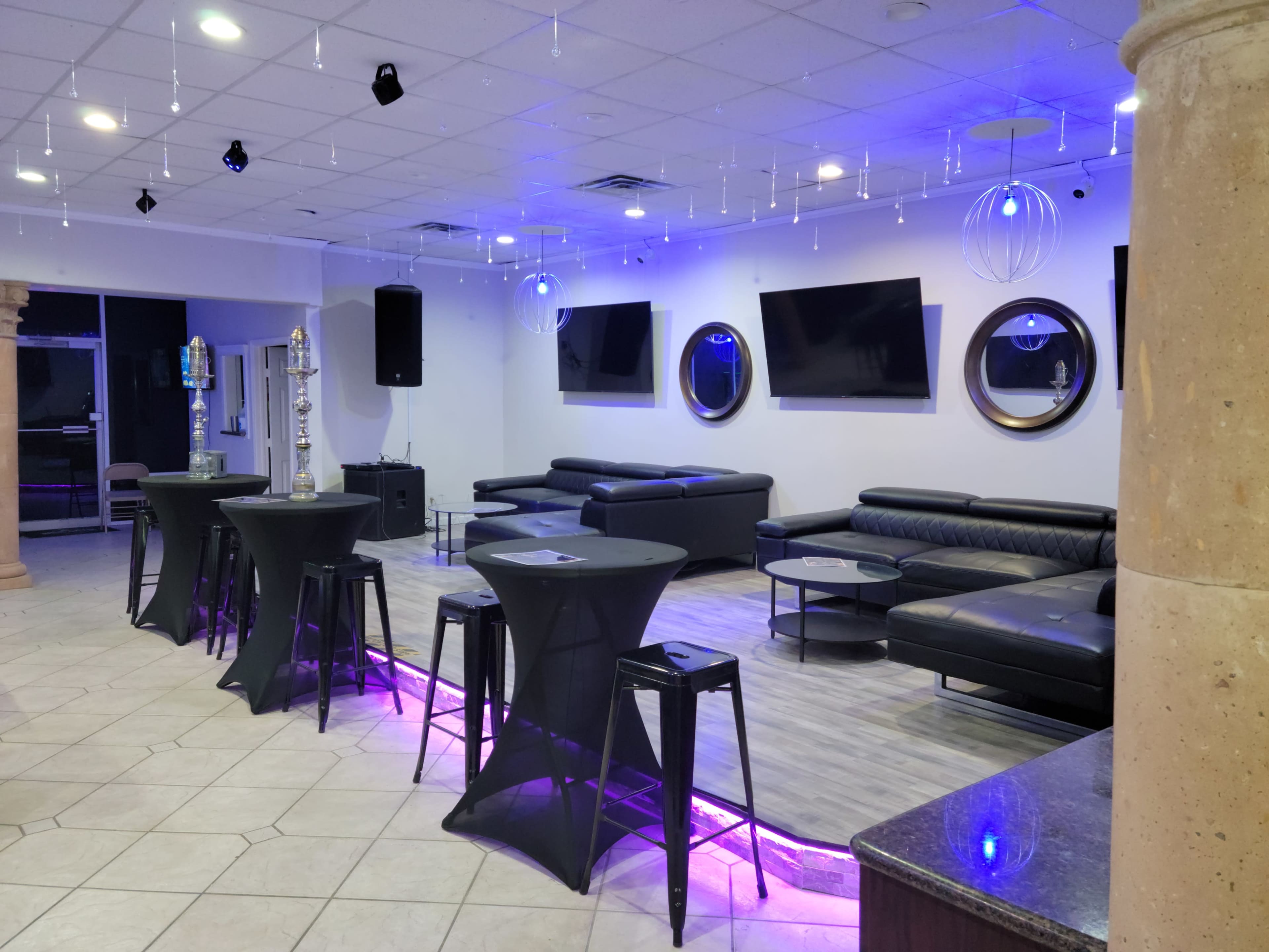 A modern lounge area with black seating, tall tables, and multiple flat-screen televisions on the walls.