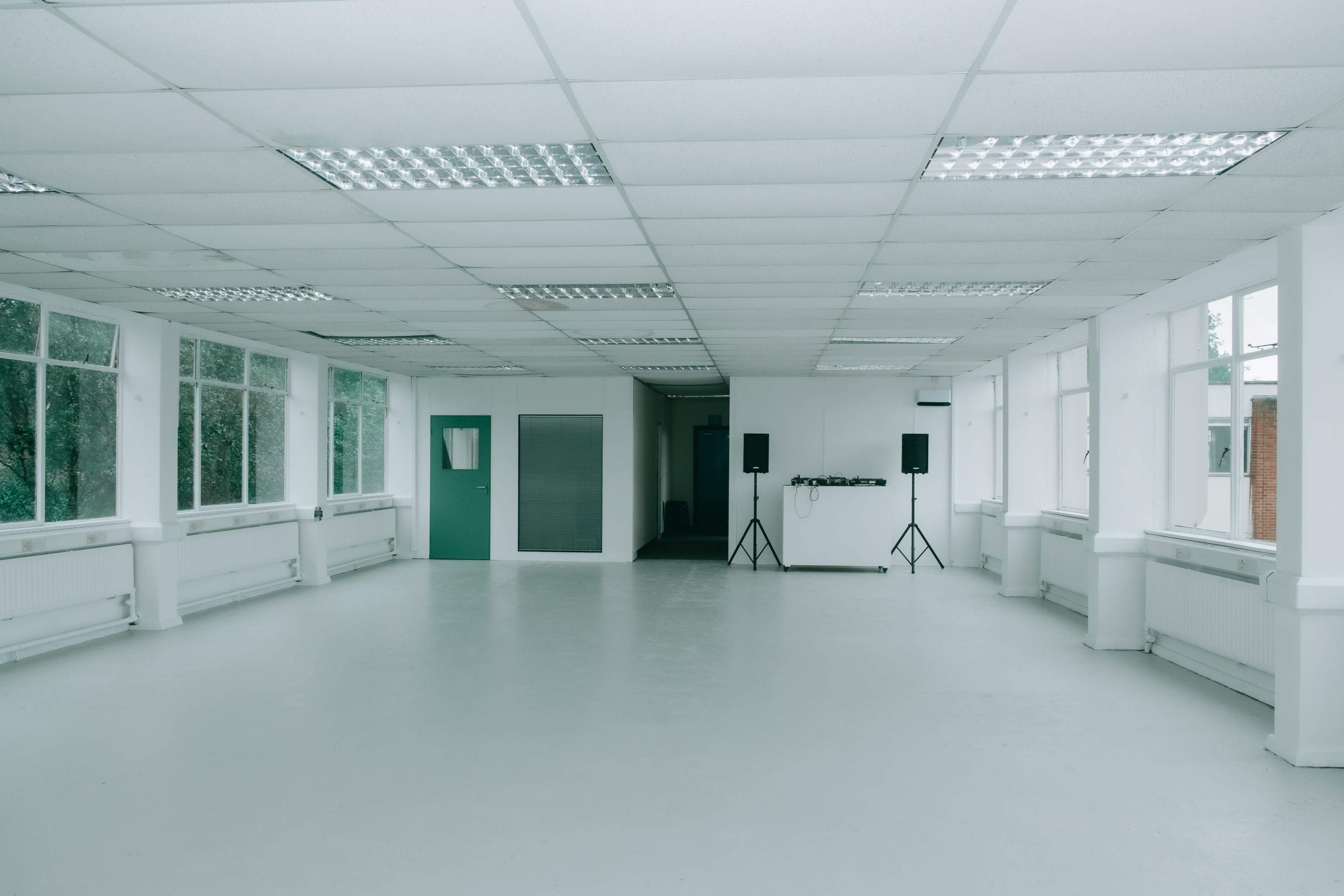 A spacious, empty room with white walls, a light gray floor, and large windows letting in natural light.