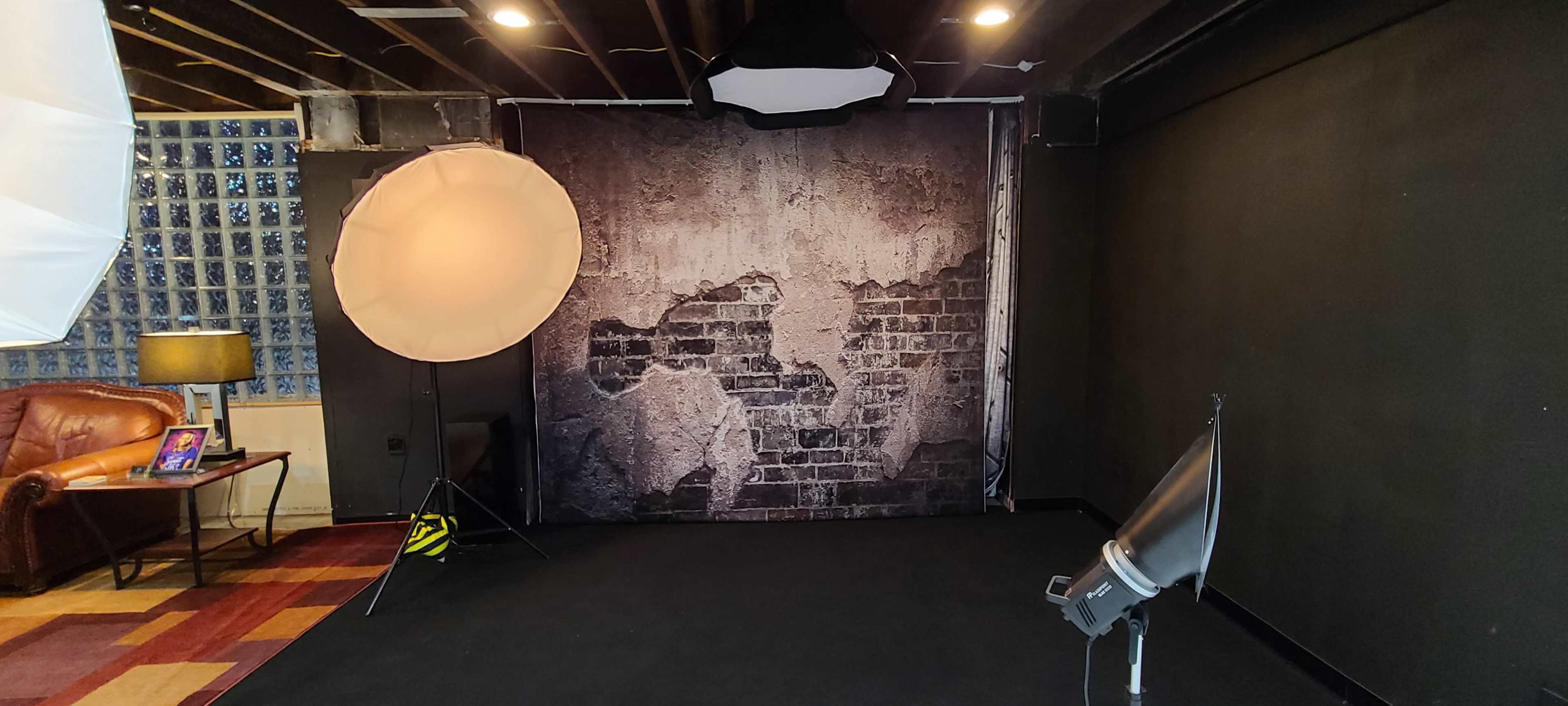 A photography studio with a textured wall backdrop, a large light umbrella, and a filming light on a black floor.