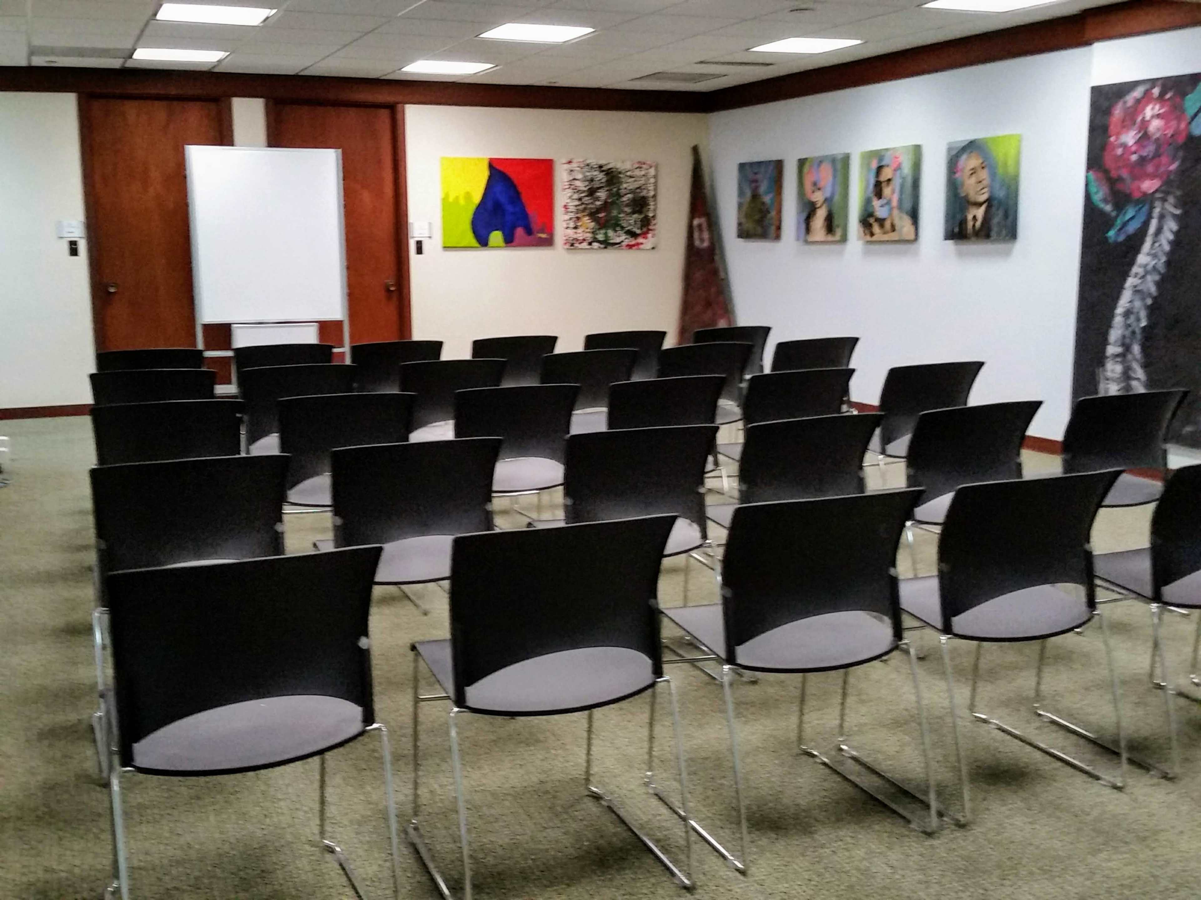 A conference room with rows of black chairs facing a whiteboard and colorful artwork on the walls.