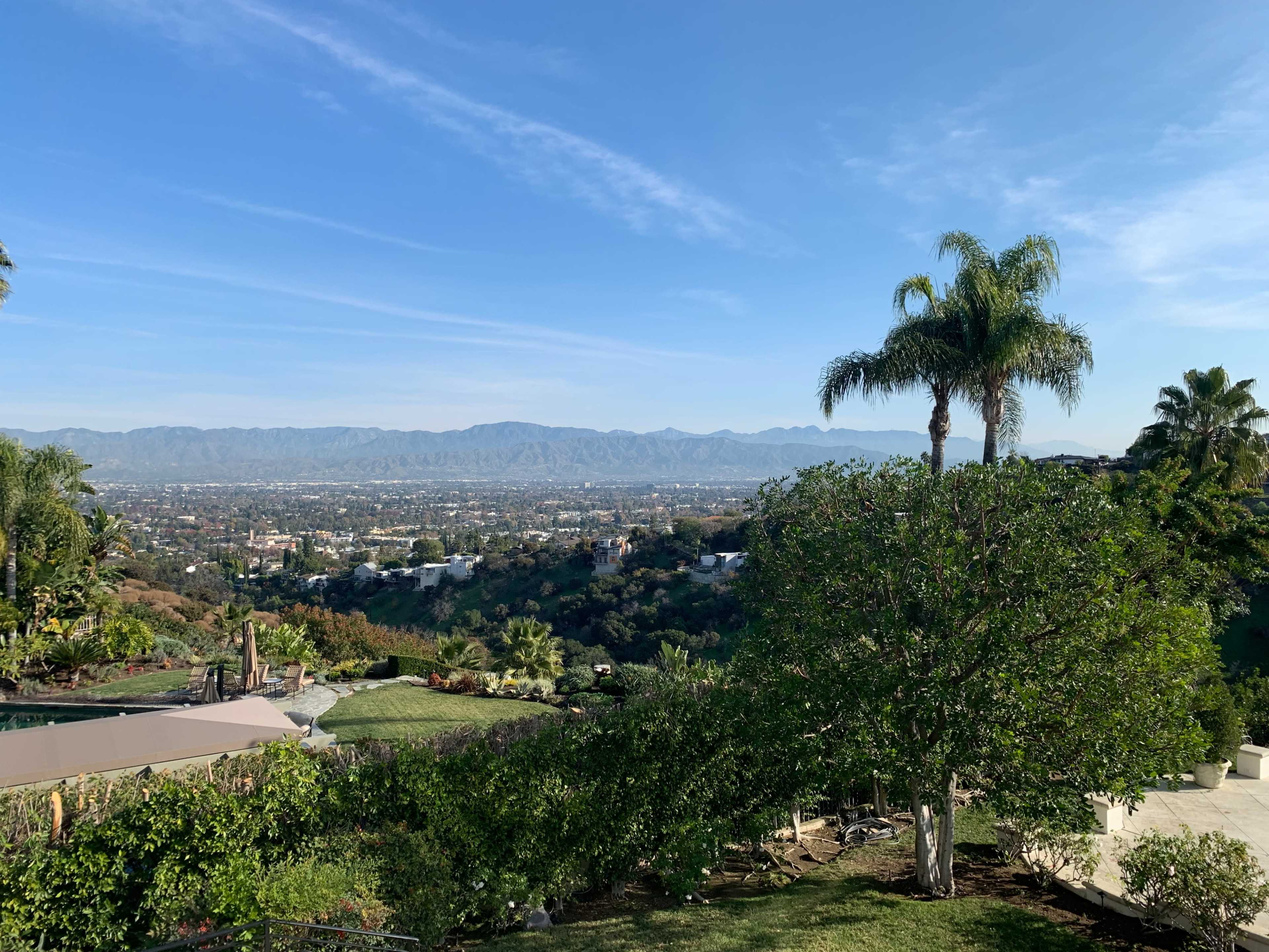 The image shows a landscaped garden with lush greenery and a view of distant mountains under a clear blue sky.