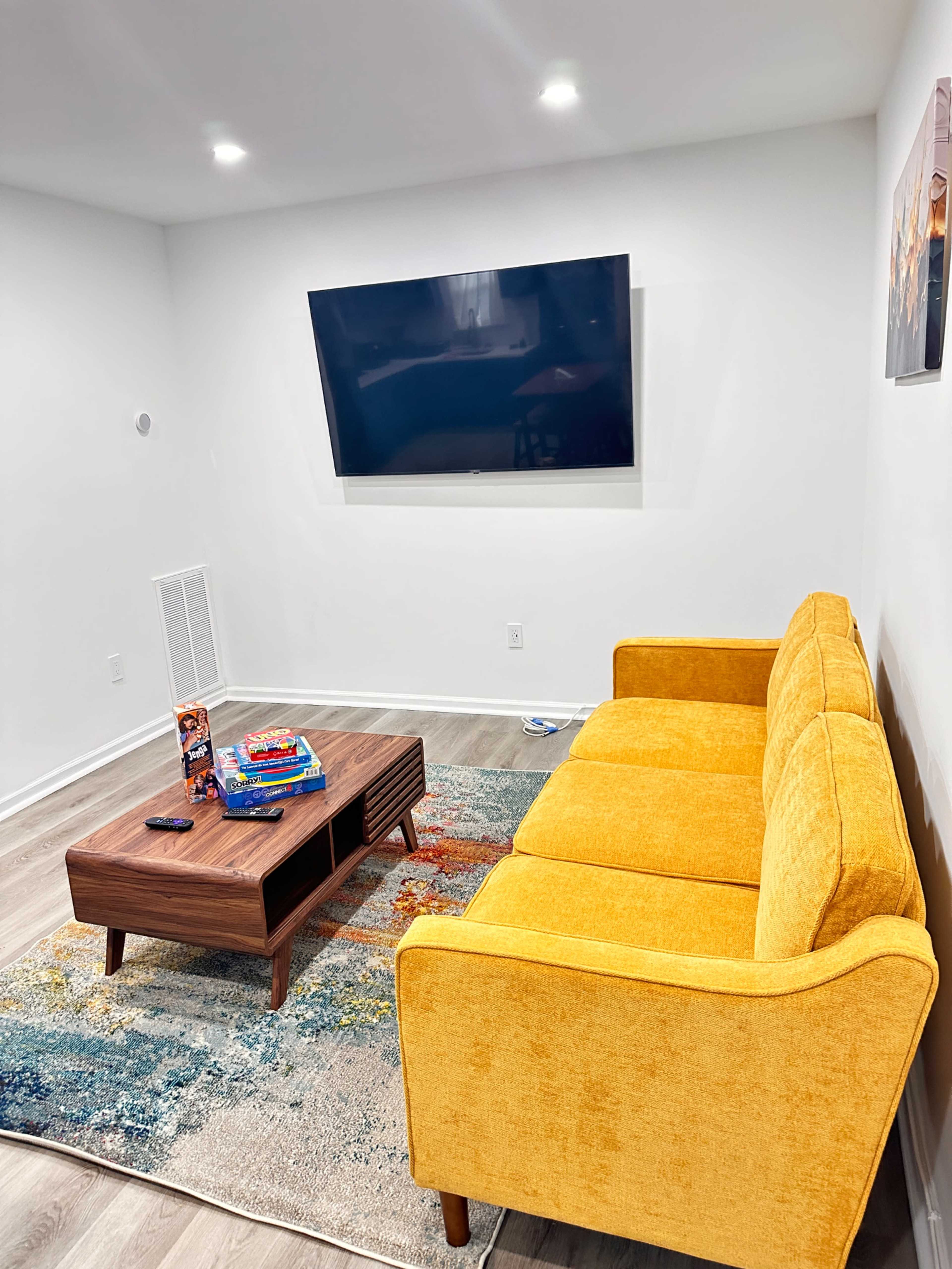 A bright yellow couch sits in a modern living room with a wooden coffee table and a wall-mounted television.