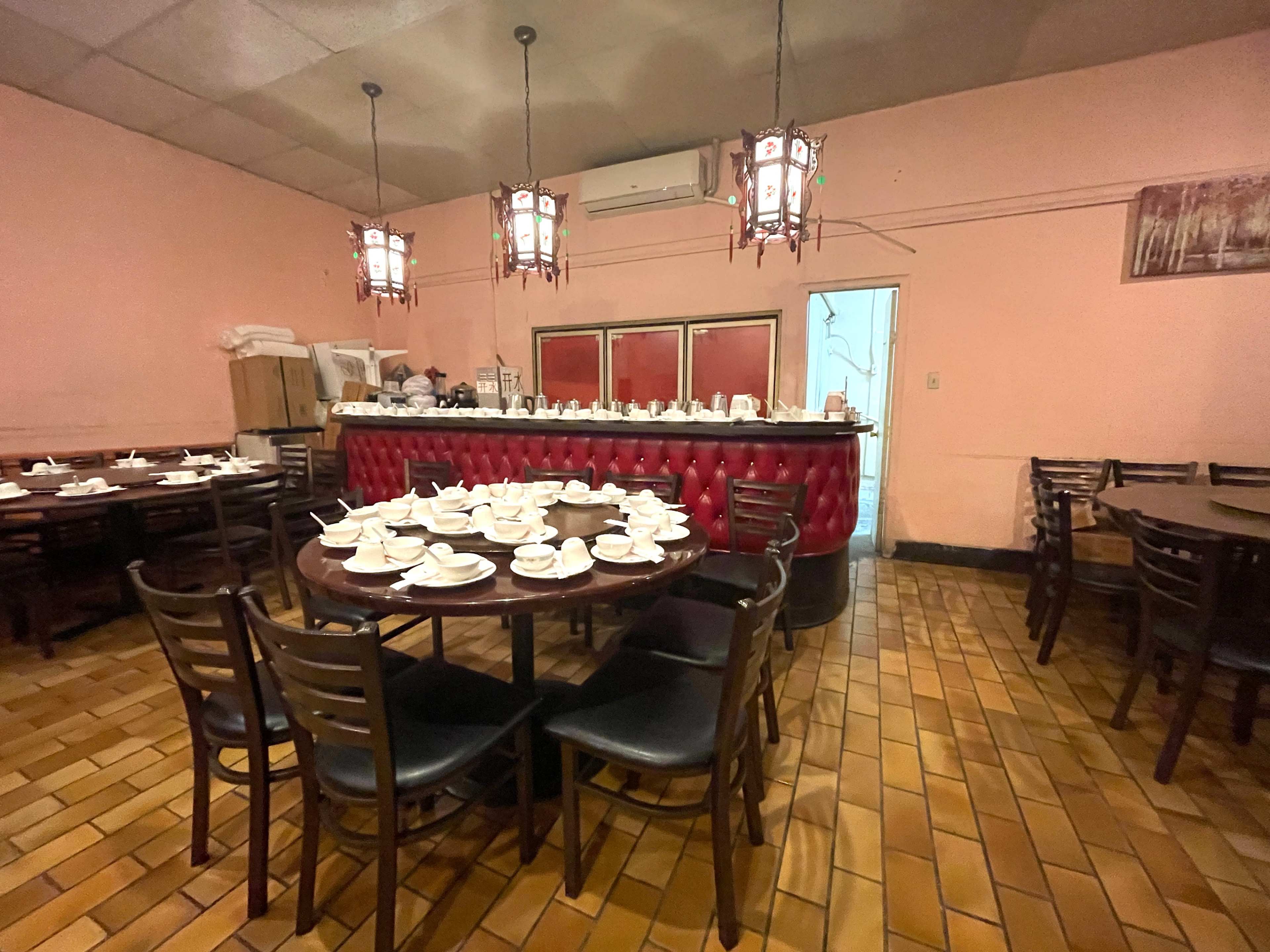 The image shows a restaurant interior featuring several round tables set with white teacups and a red cushioned counter in the background.