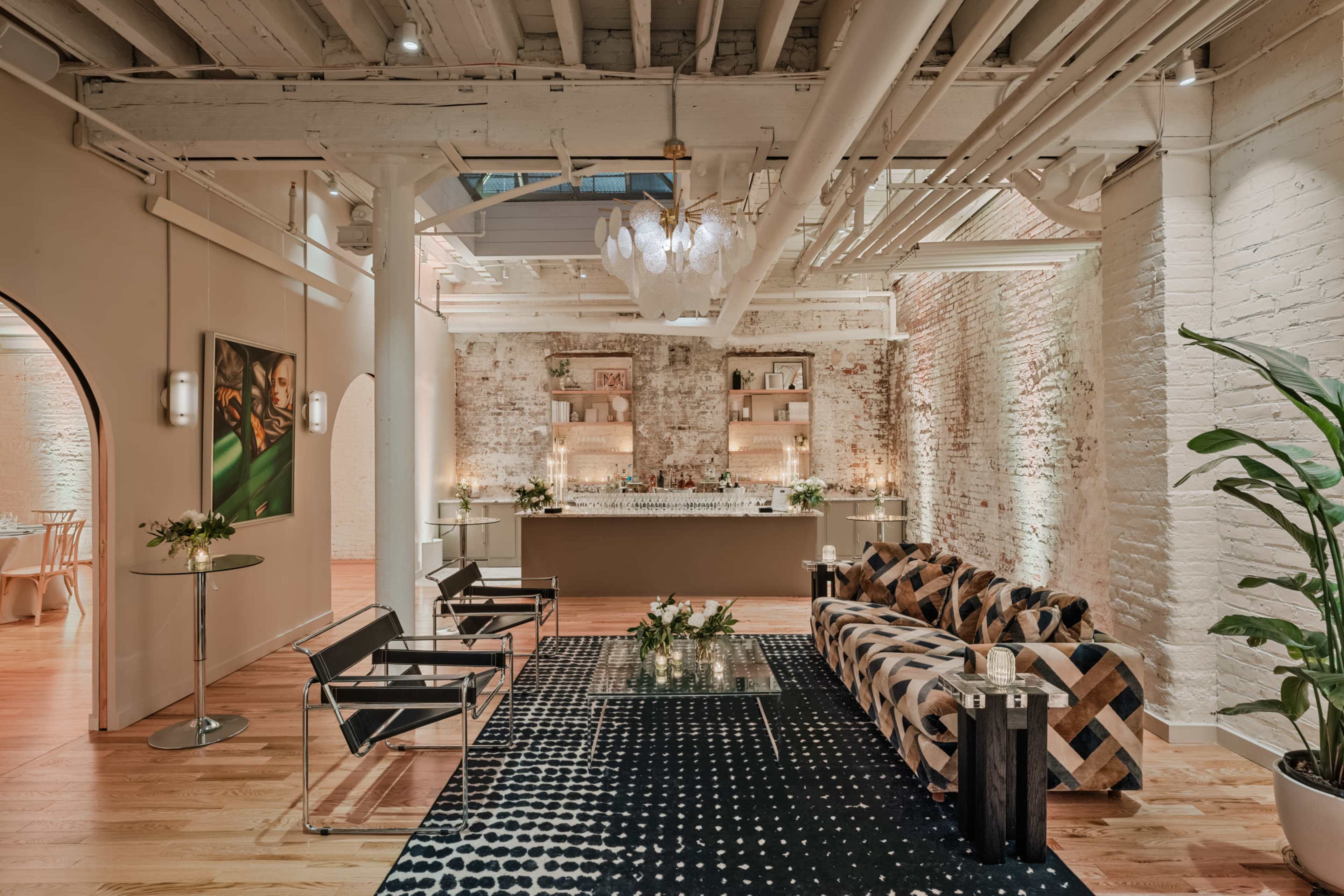 A modern interior space featuring a lounge area with a patterned sofa, glass coffee table, and a bar counter in the background, illuminated by soft lighting.
