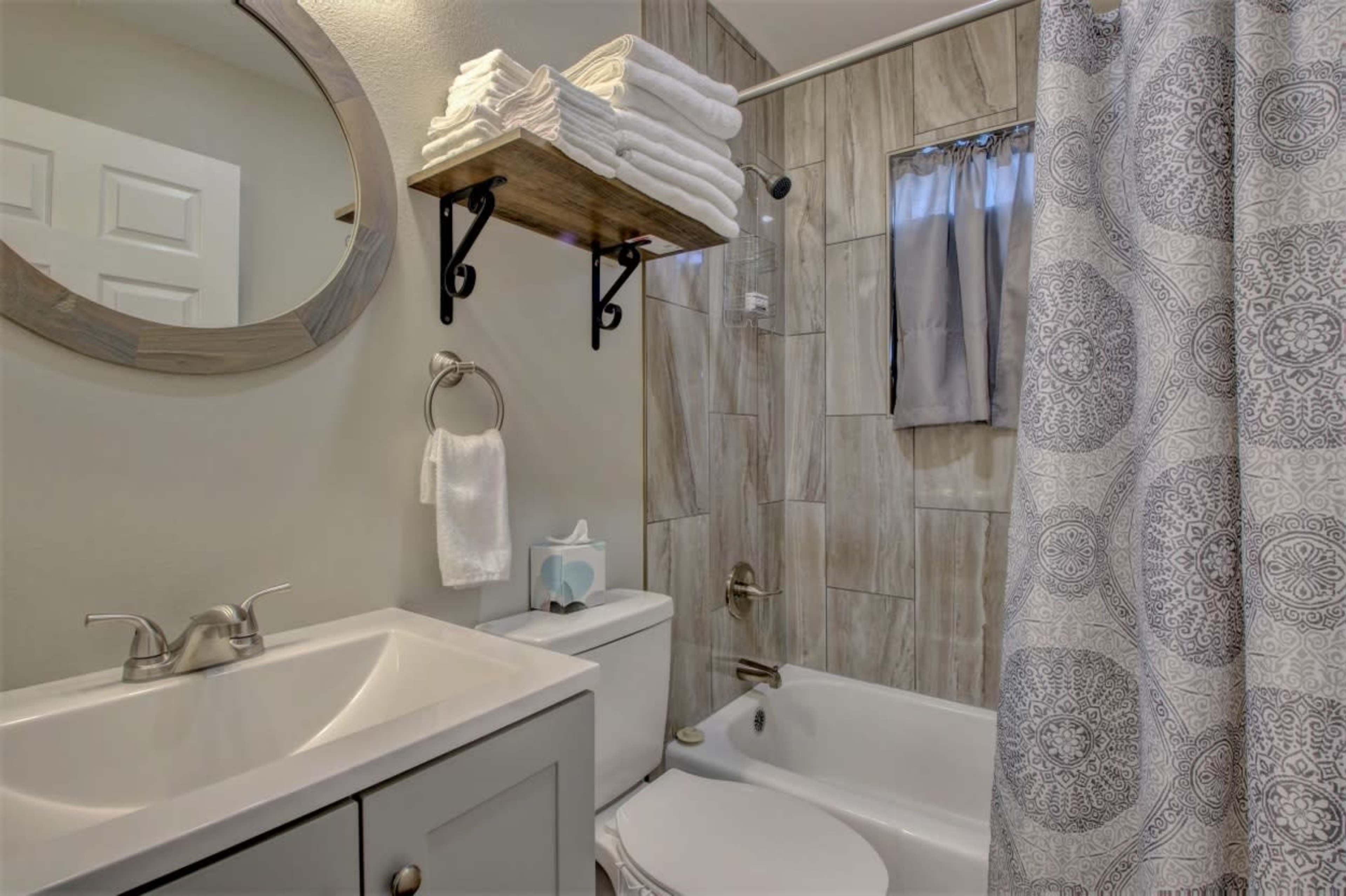 A modern bathroom featuring a bathtub with a shower curtain, a vanity with a sink, and neatly stacked towels on a shelf.
