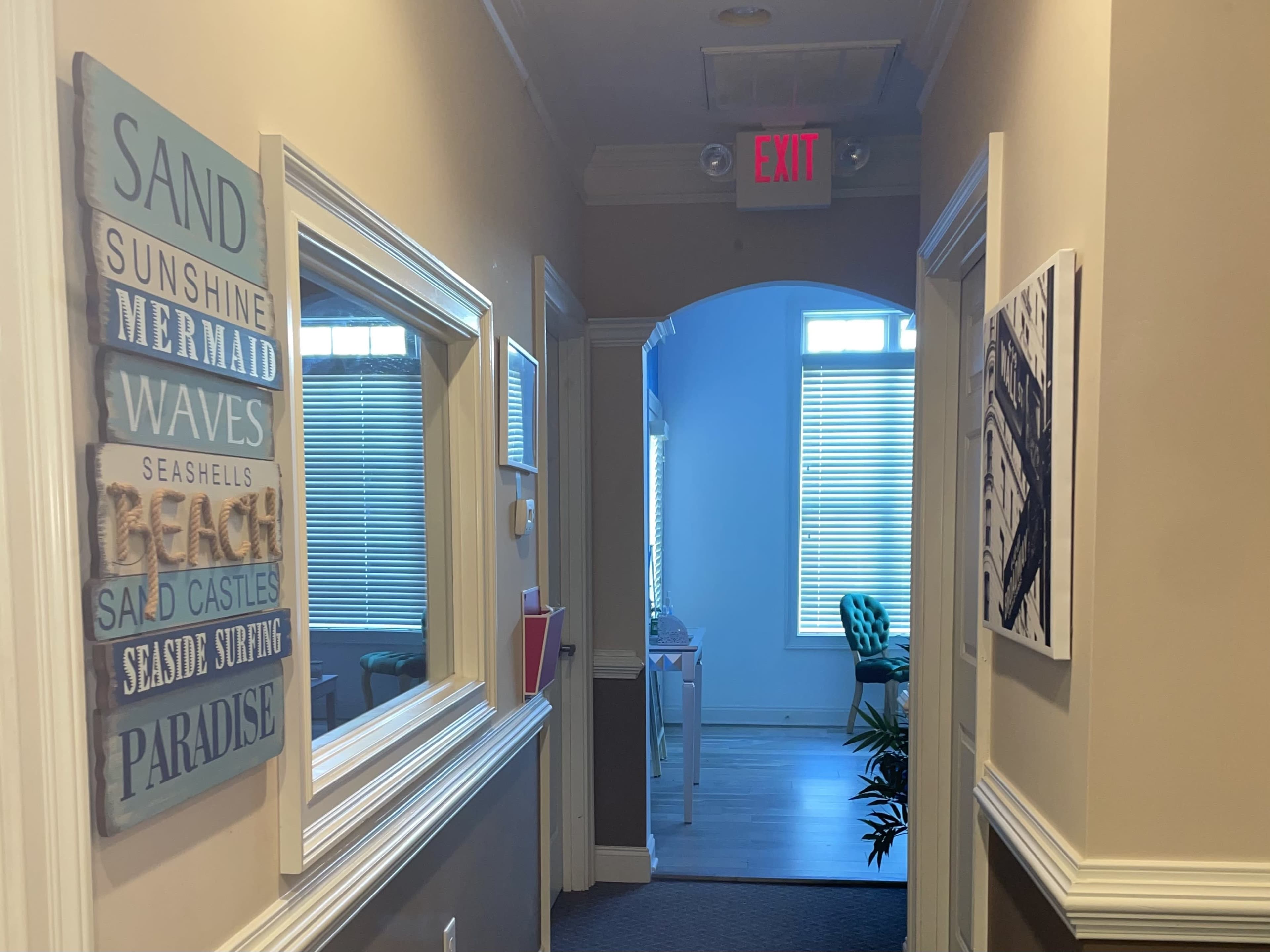 A hallway features decorative wall art and a door leading to a well-lit room at the end.