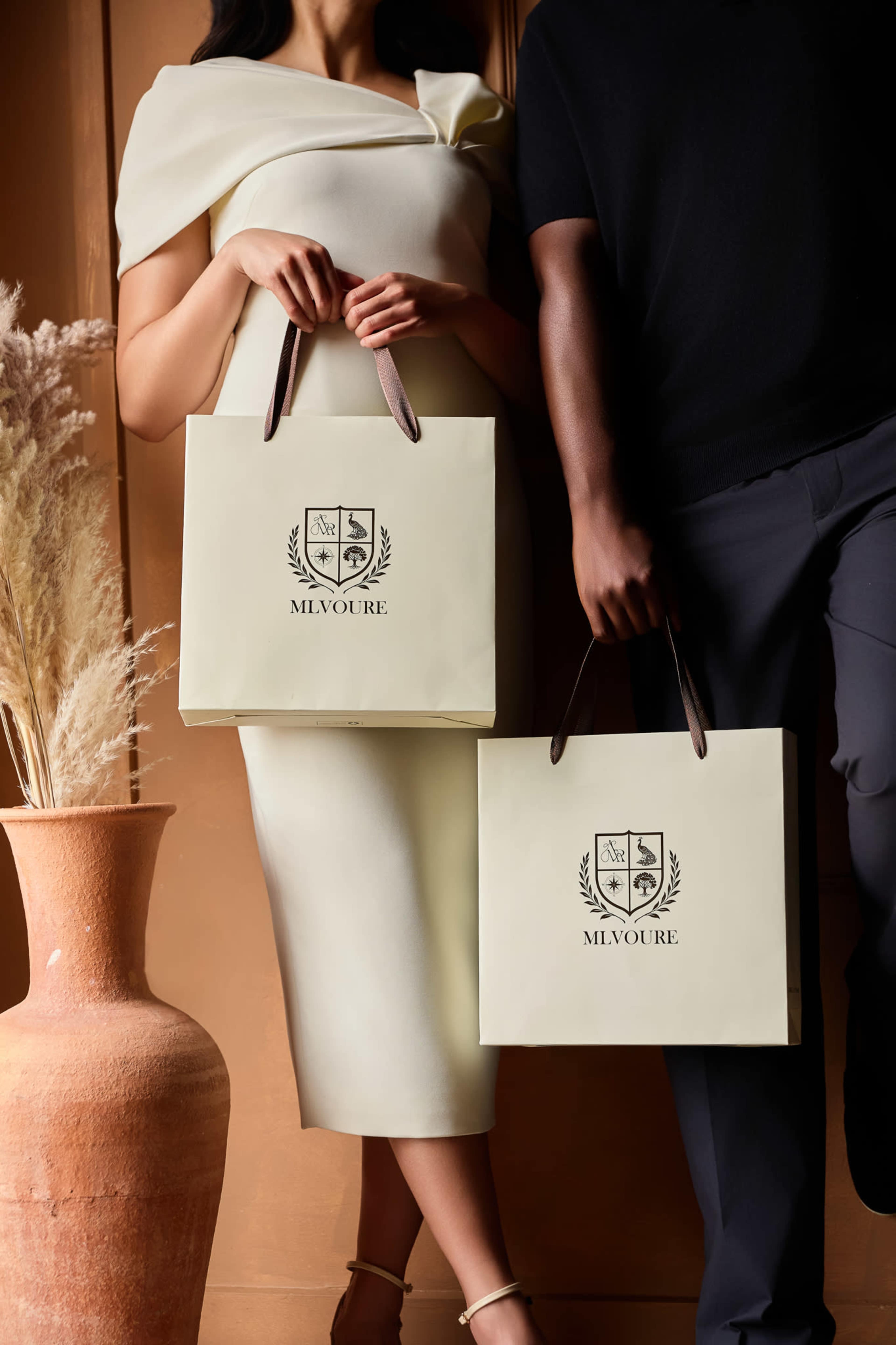 A person in a white dress and another person in a black shirt hold matching shopping bags in front of a neutral-toned wall and a decorative vase.