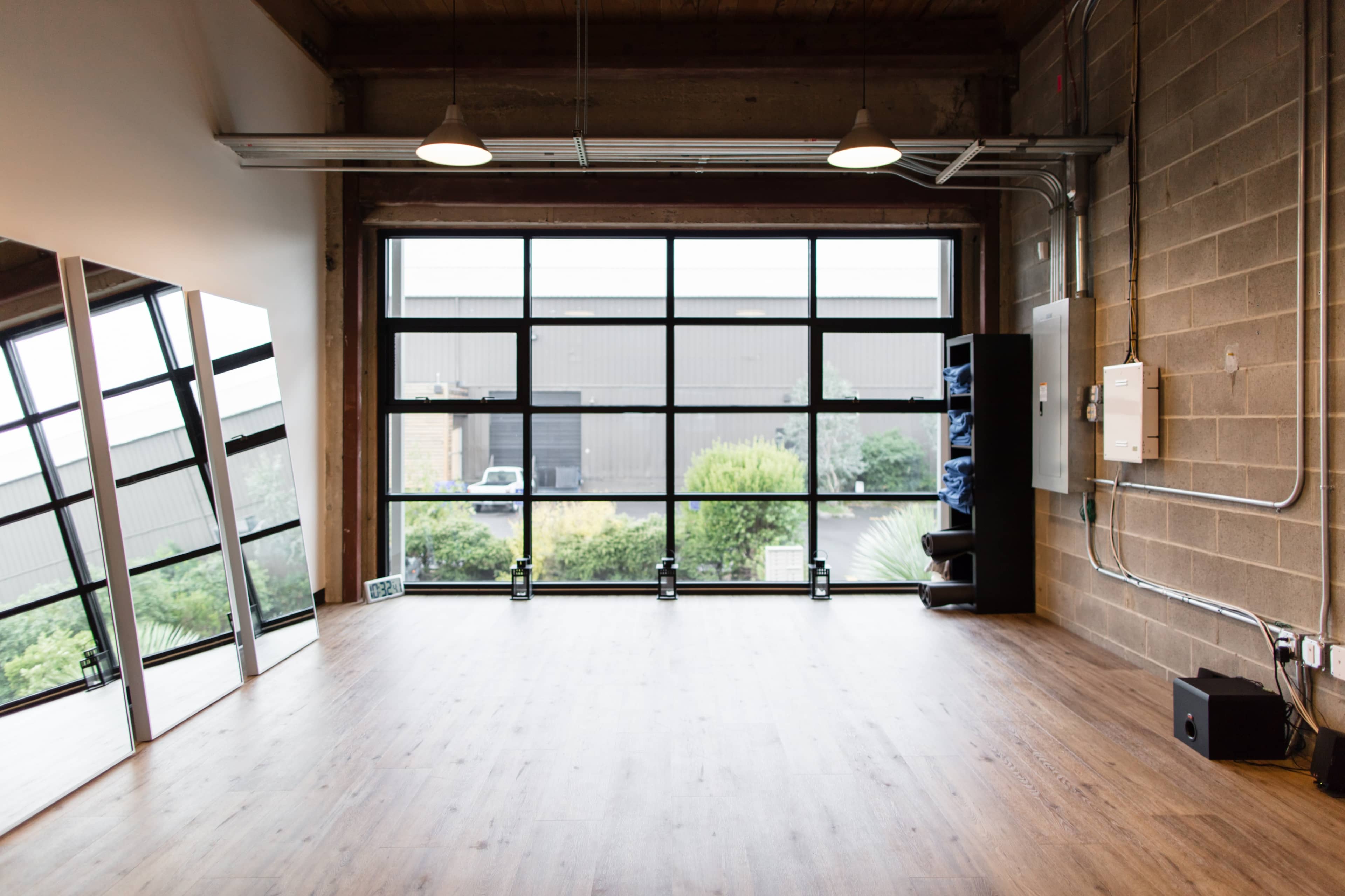 A spacious room with large windows, wooden flooring, and a wall with mirrors and storage.