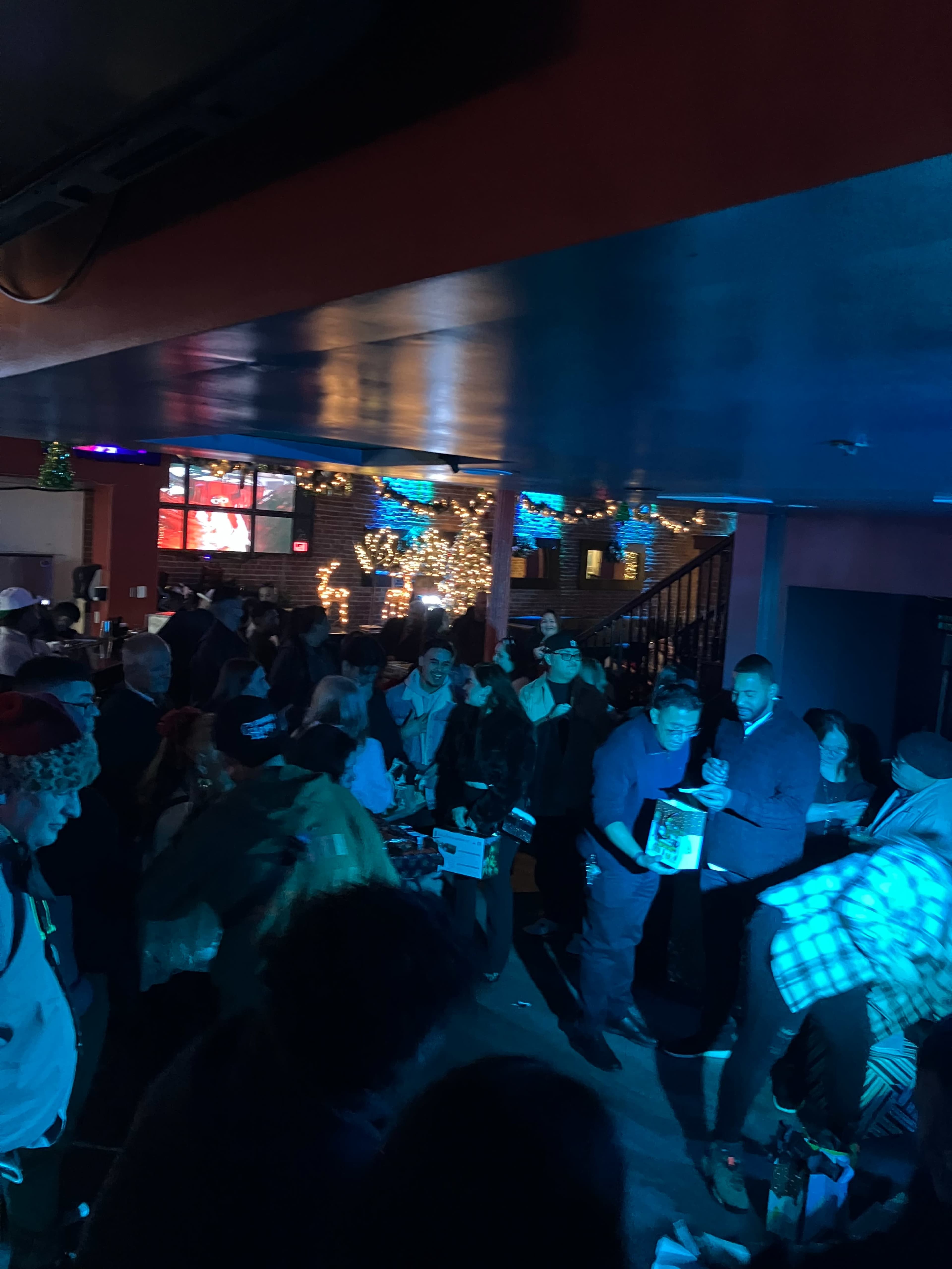 A crowded indoor venue is filled with people socializing under colorful lighting and decorations.