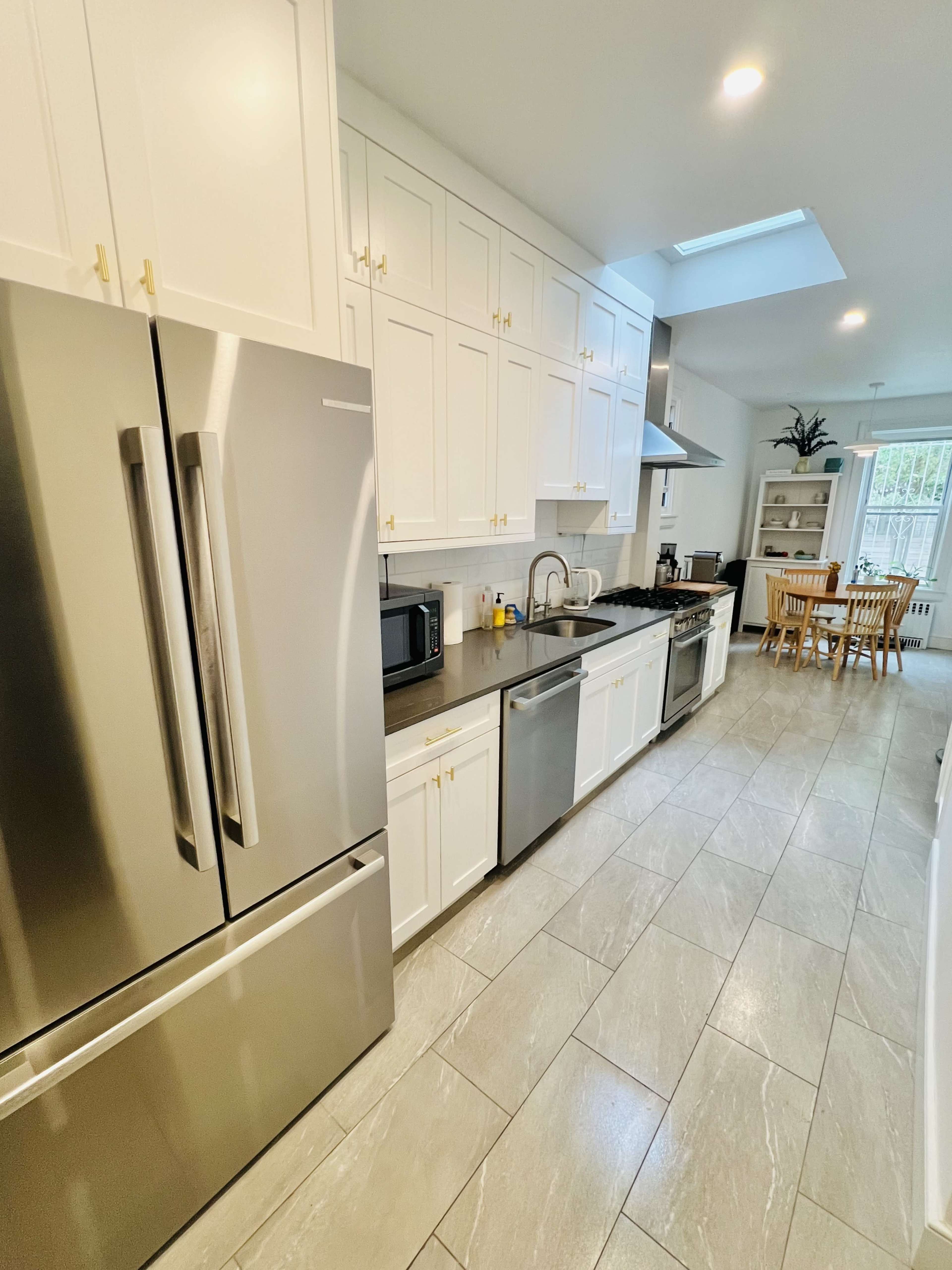 A modern kitchen features stainless steel appliances, white cabinetry, and a dining area with a wooden table and chairs.