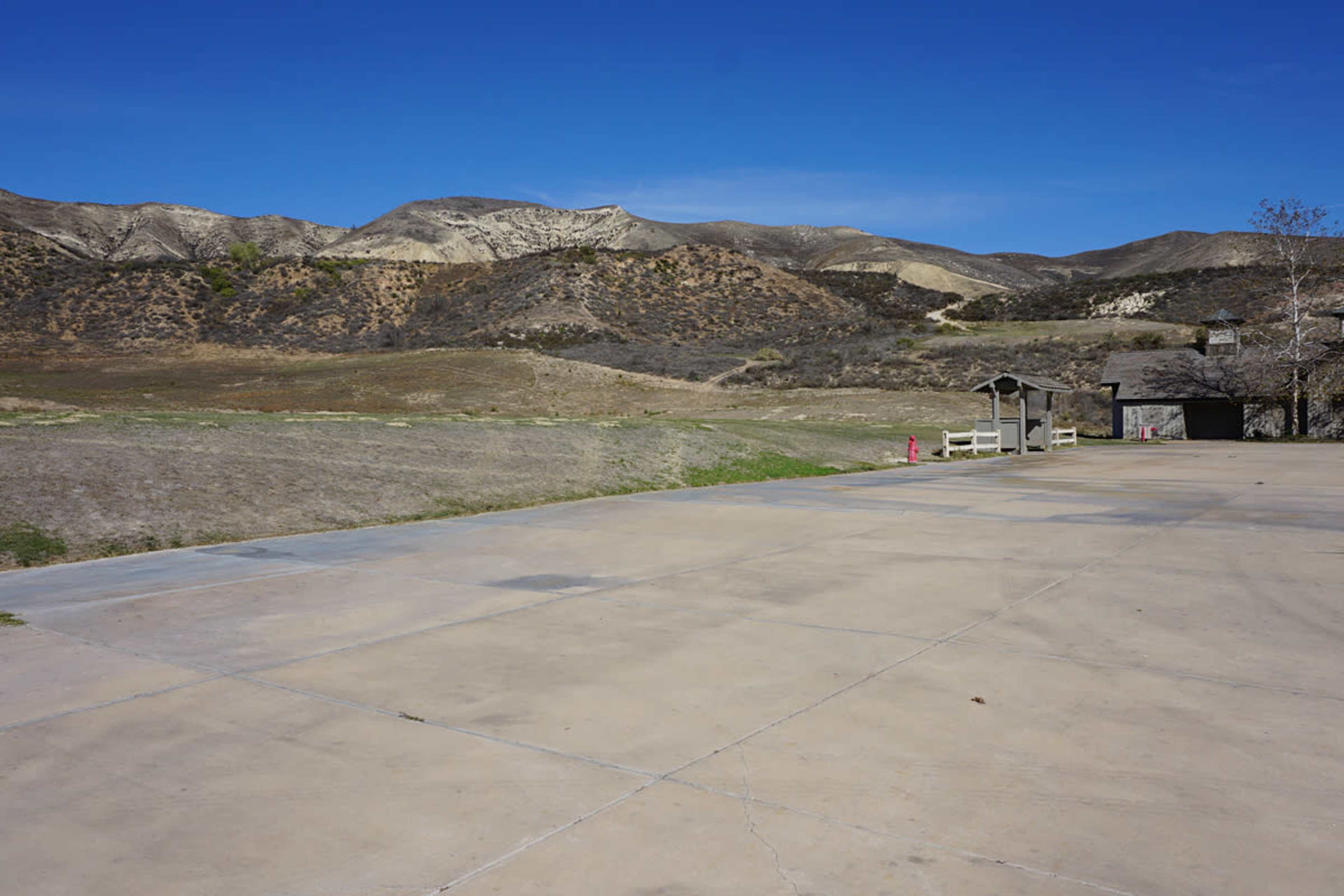 The image shows a wide concrete area with a view of dry, mountainous terrain in the background under a clear blue sky.
