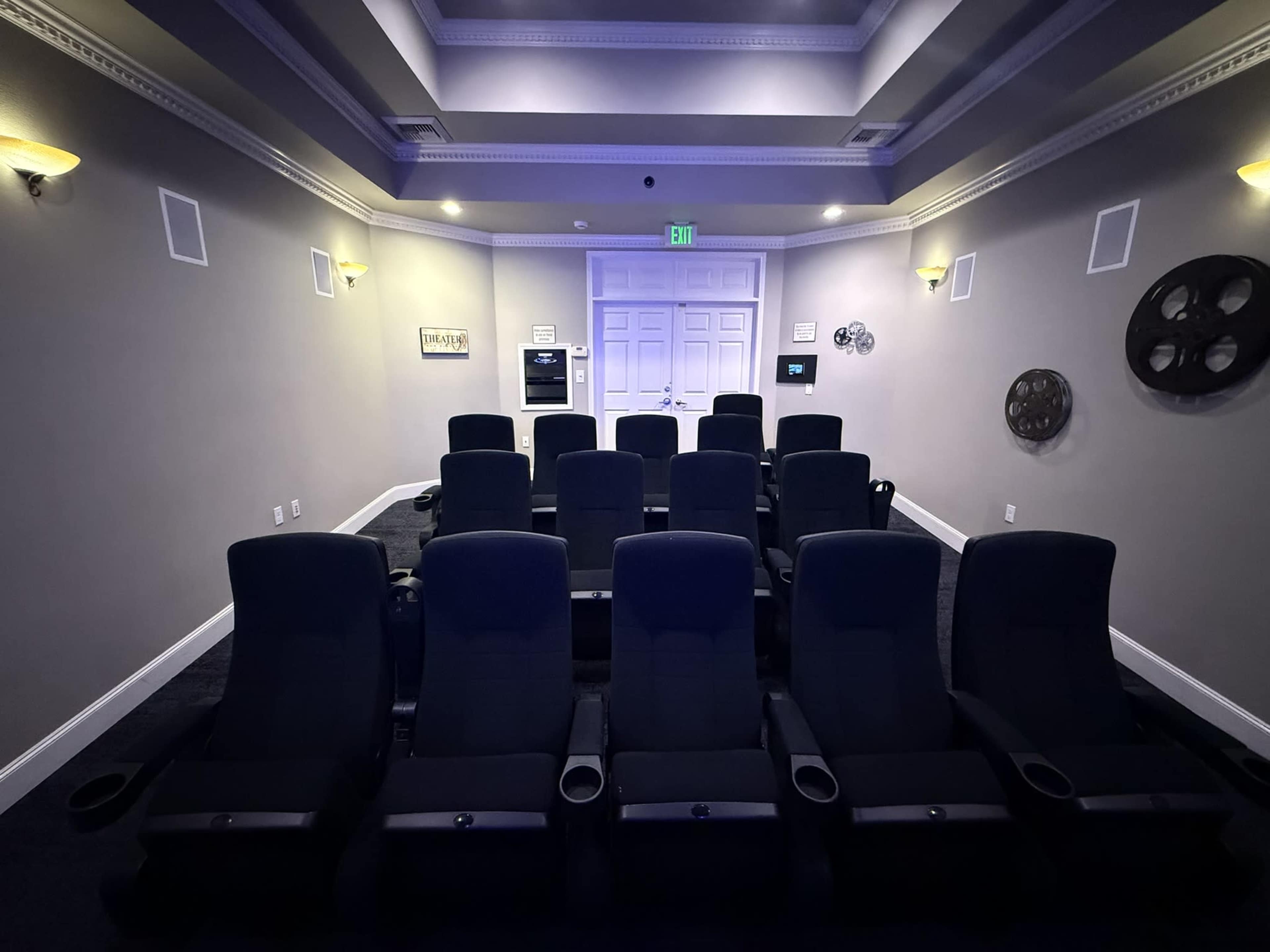The image shows a small, dimly lit home theater with several rows of reclining chairs facing a screen.