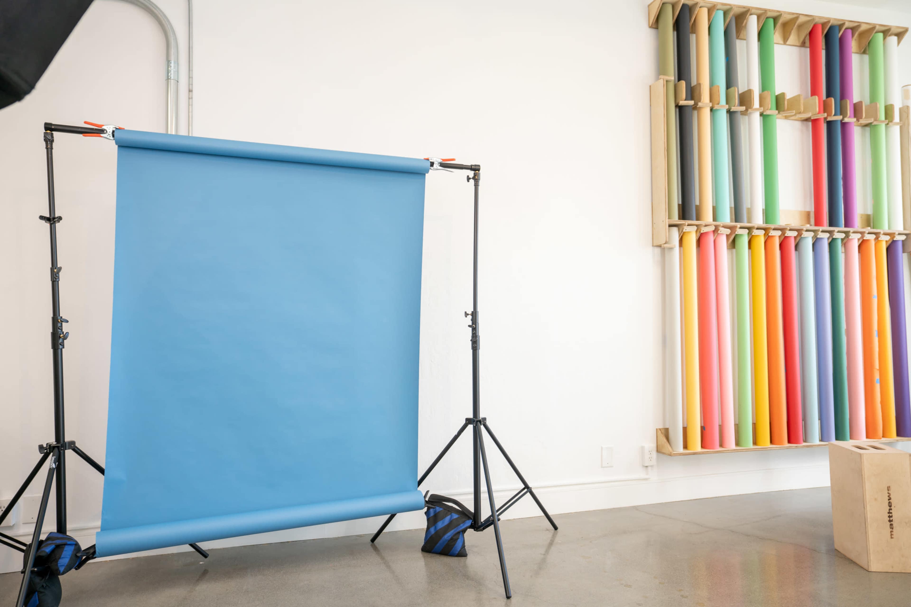 A blue backdrop is set up on a stand next to a wall displaying rolls of colorful paper in various shades.