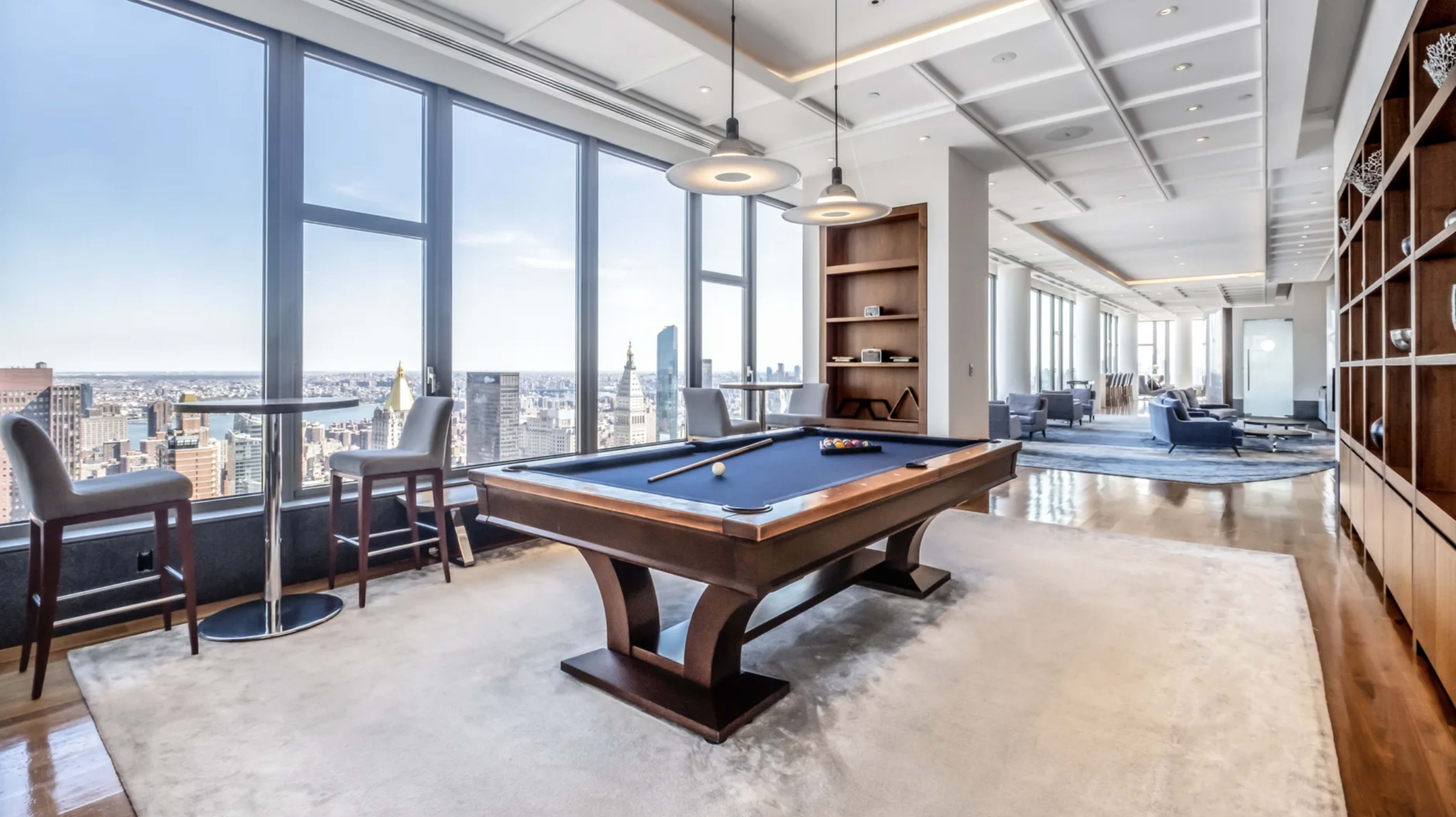 A game room featuring a pool table with large windows overlooking a city skyline.