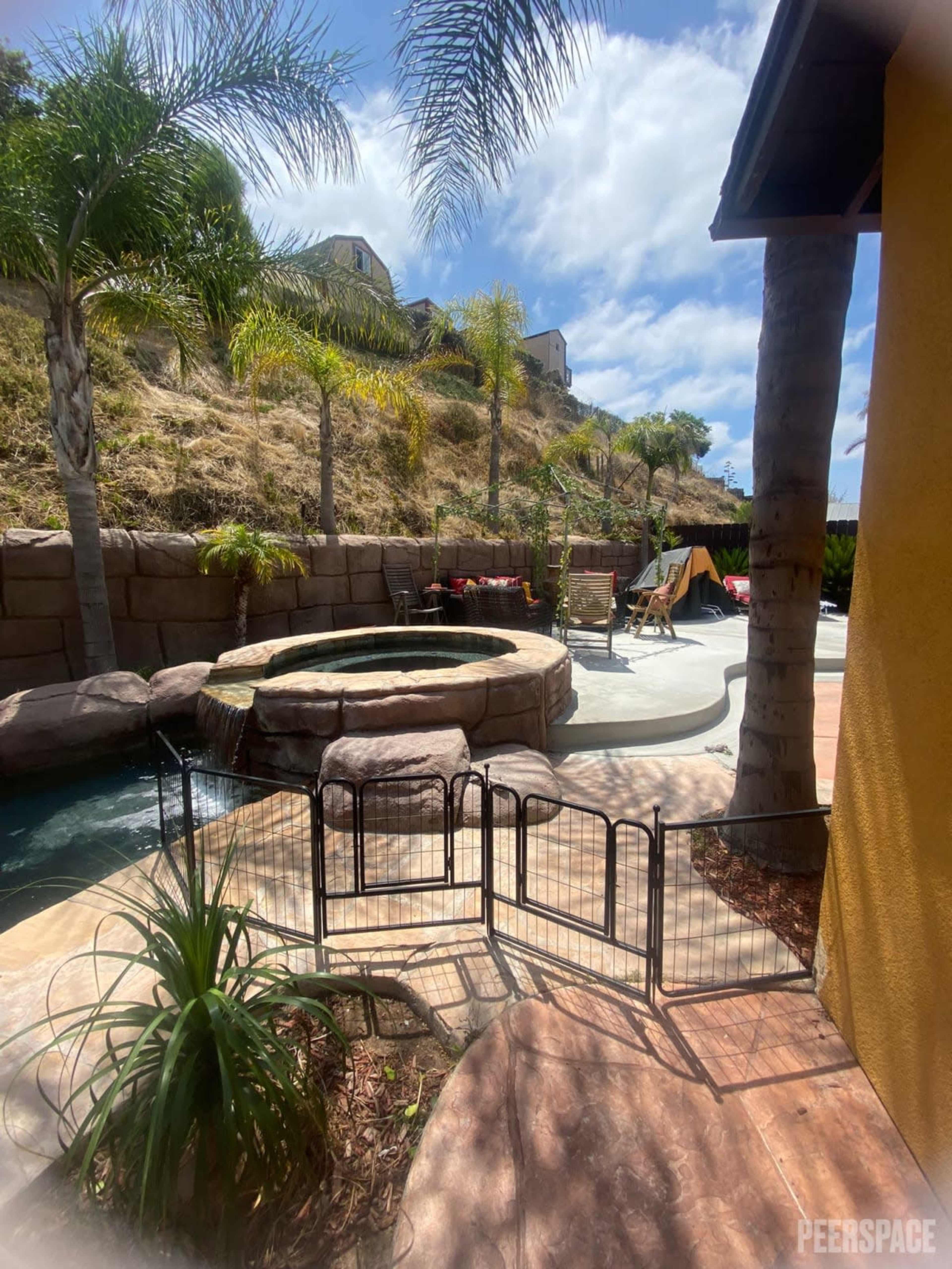 A backyard pool area with a hot tub, palm trees, and a fenced-off section on a sunny day.