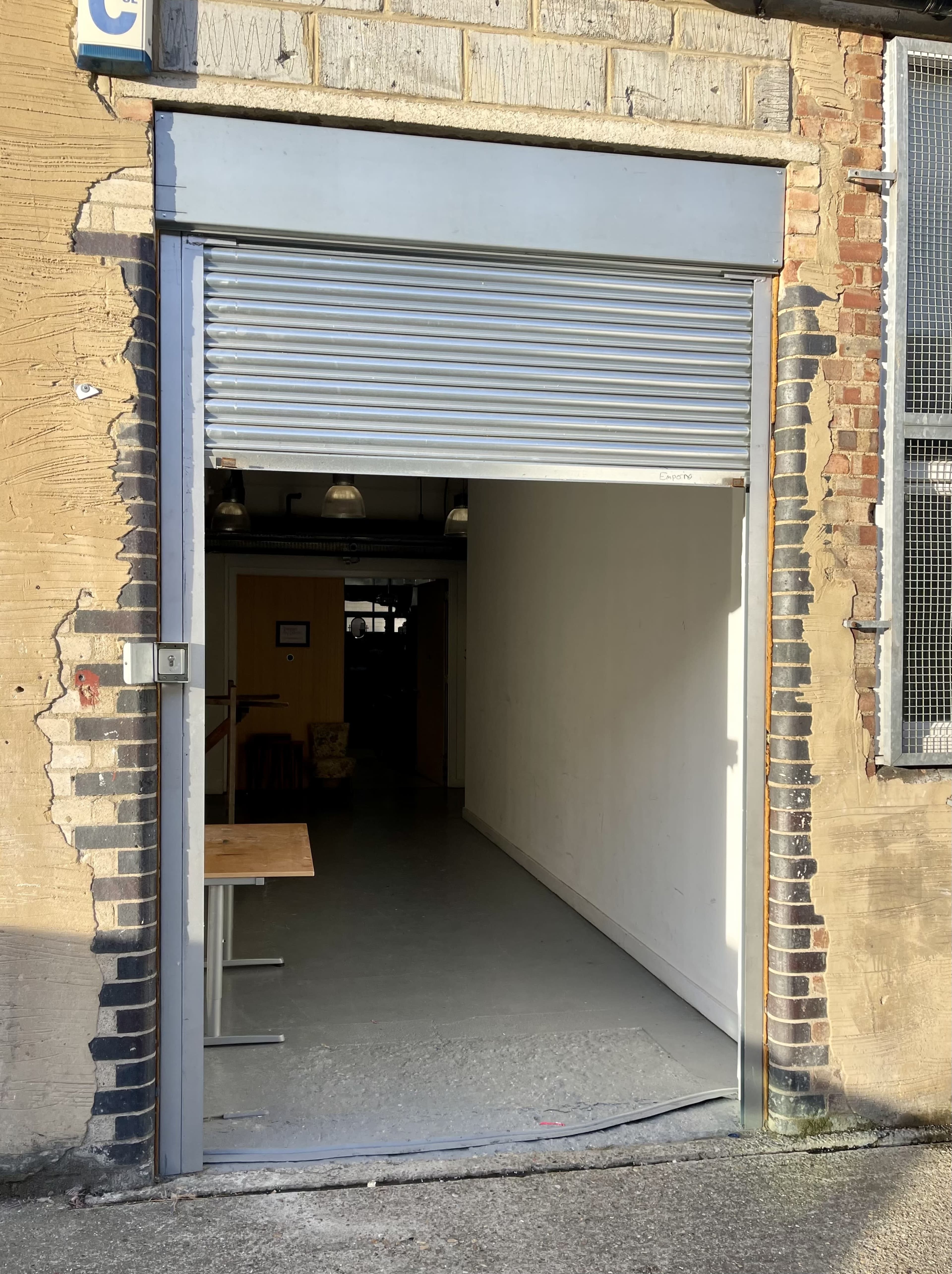 An open roll-up door leading to a narrow, well-lit corridor with a table on the left side.