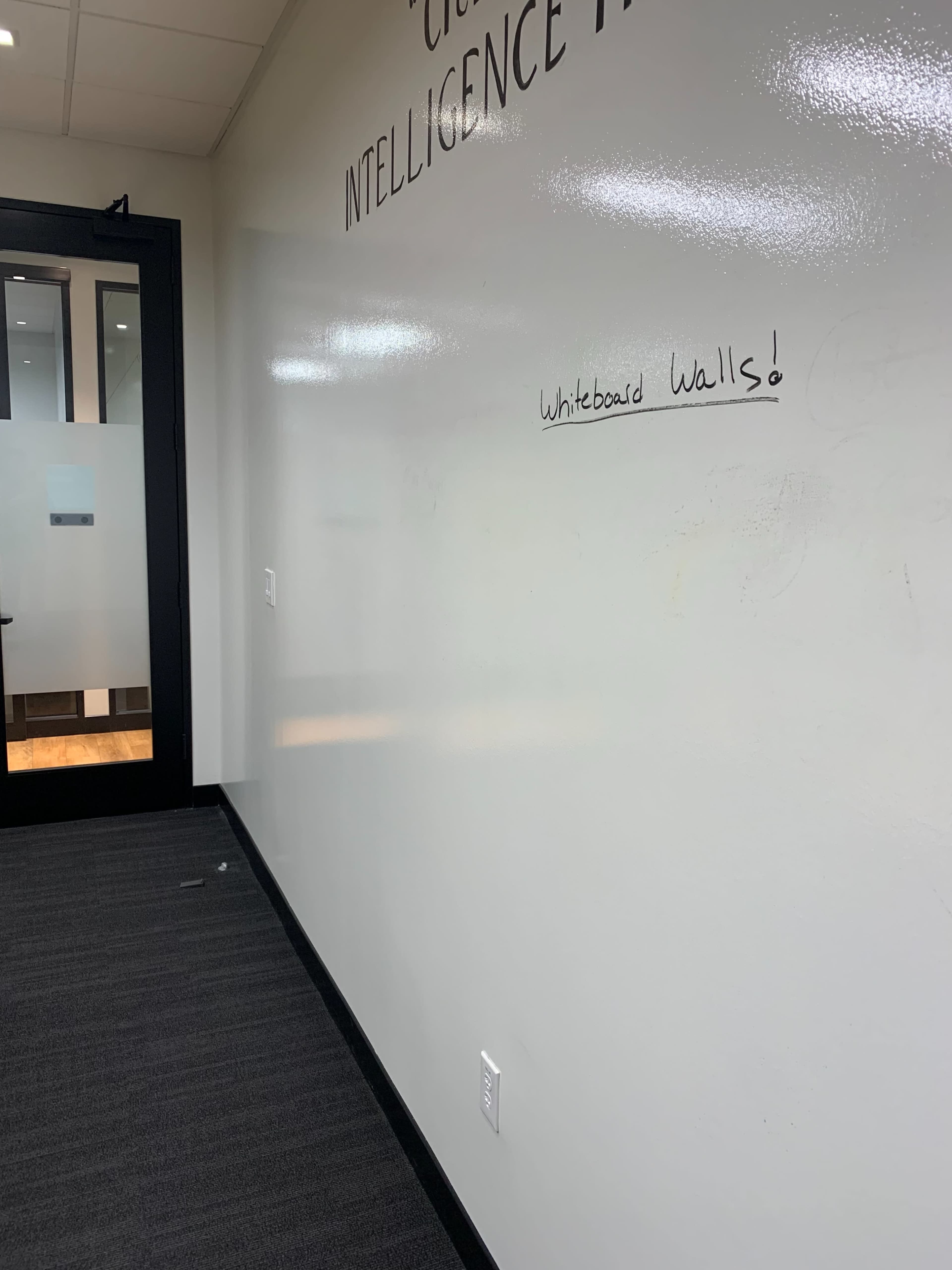 A blank white wall inside an office space with the text "Whiteboard Walls!" written on it.