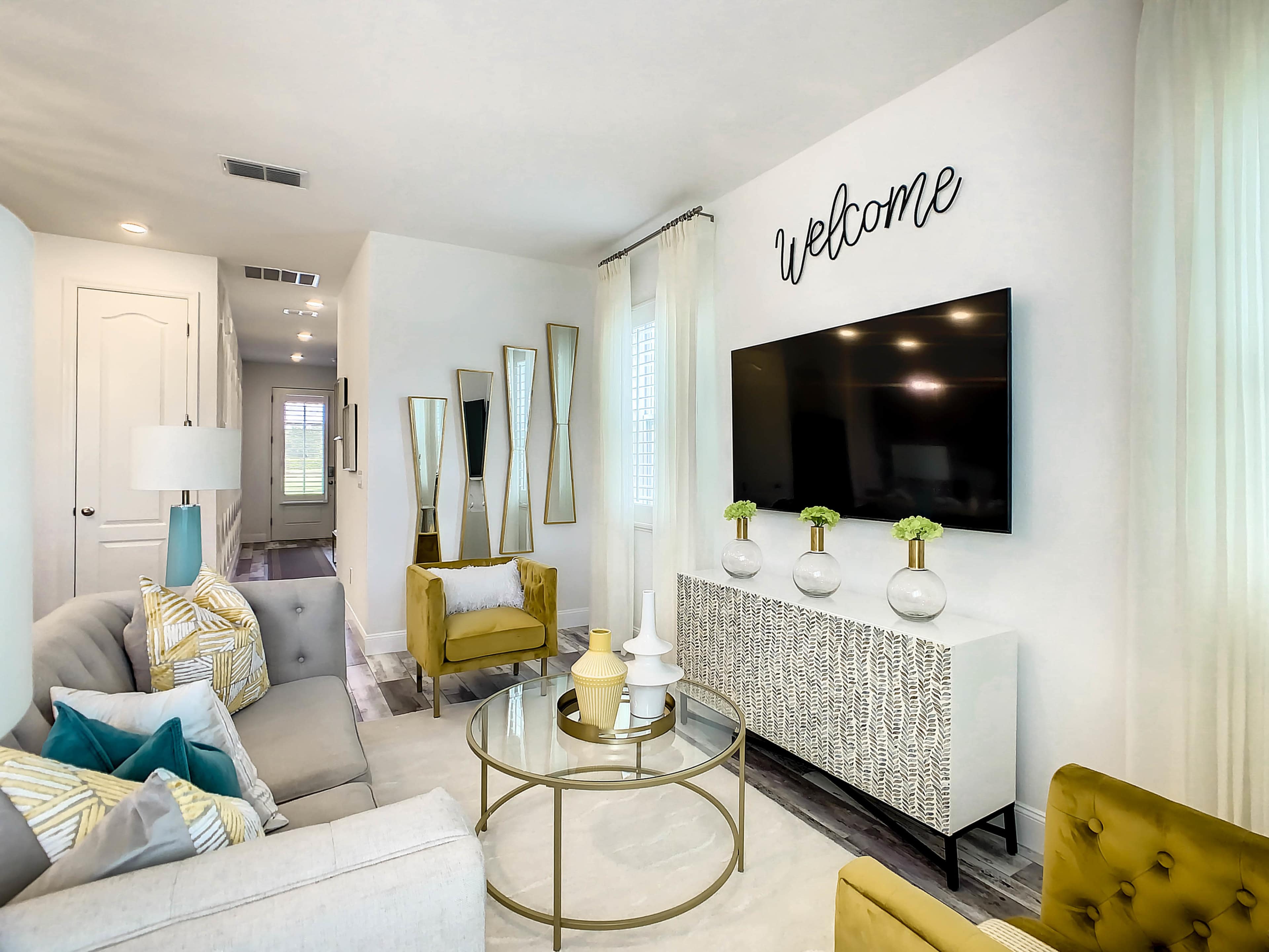 A modern living room features a large television mounted on the wall, a coffee table in the center, and a seating arrangement with a sofa and armchairs.