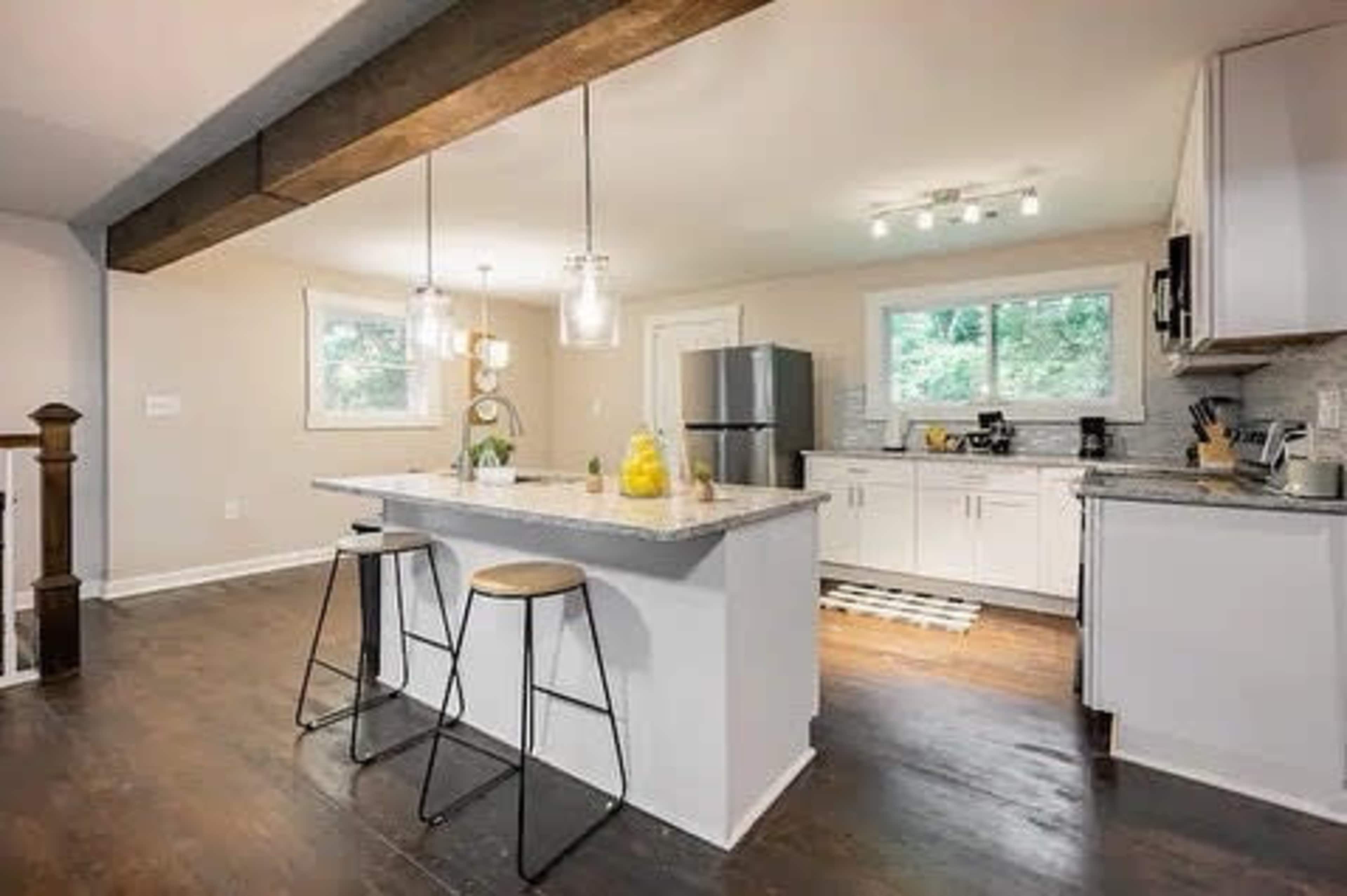A modern kitchen features a central island with two stools, white cabinetry, and stainless steel appliances.