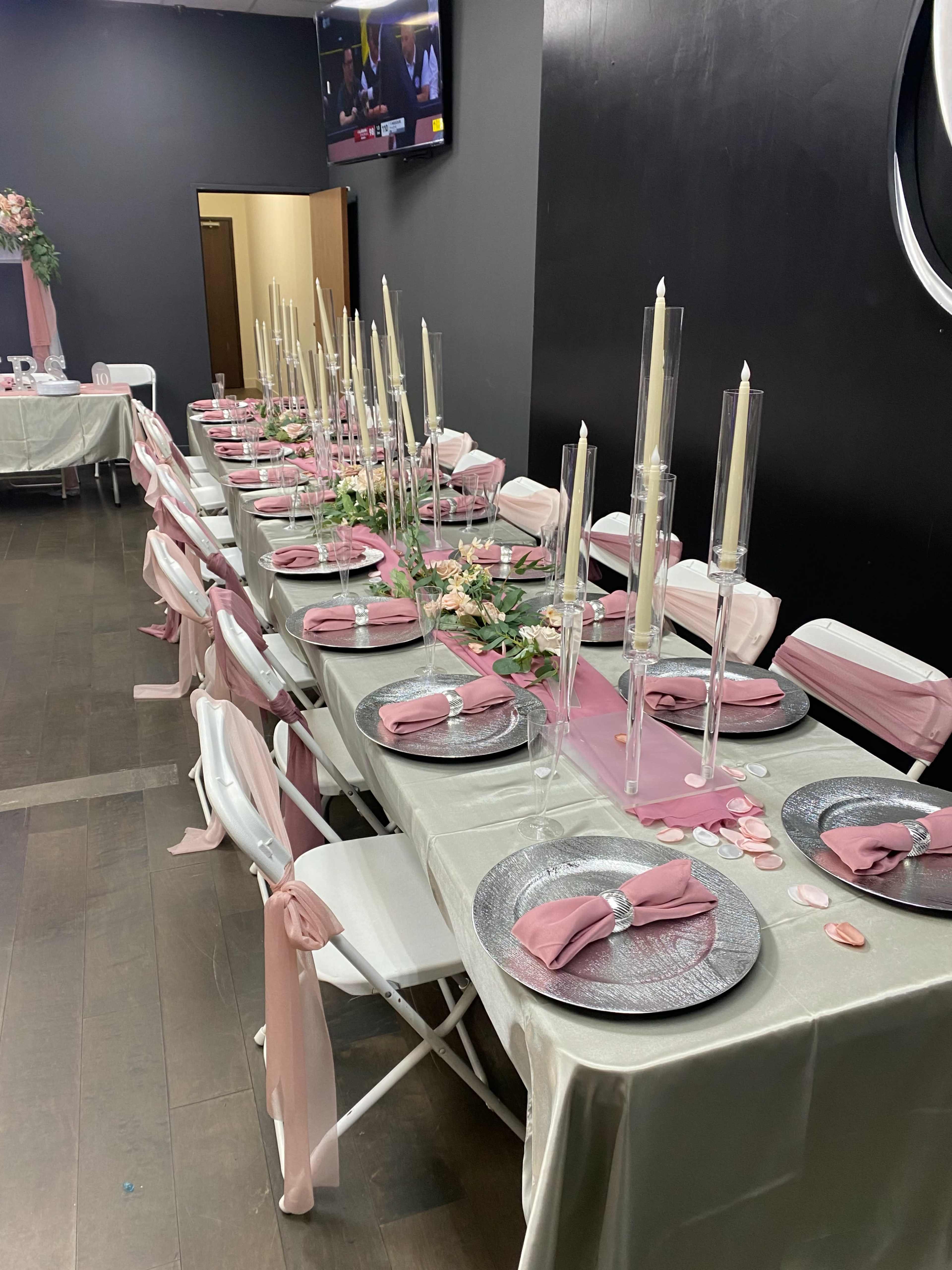 A long dining table is set with elegant place settings, tall candle holders, and floral decorations in a dimly lit room.