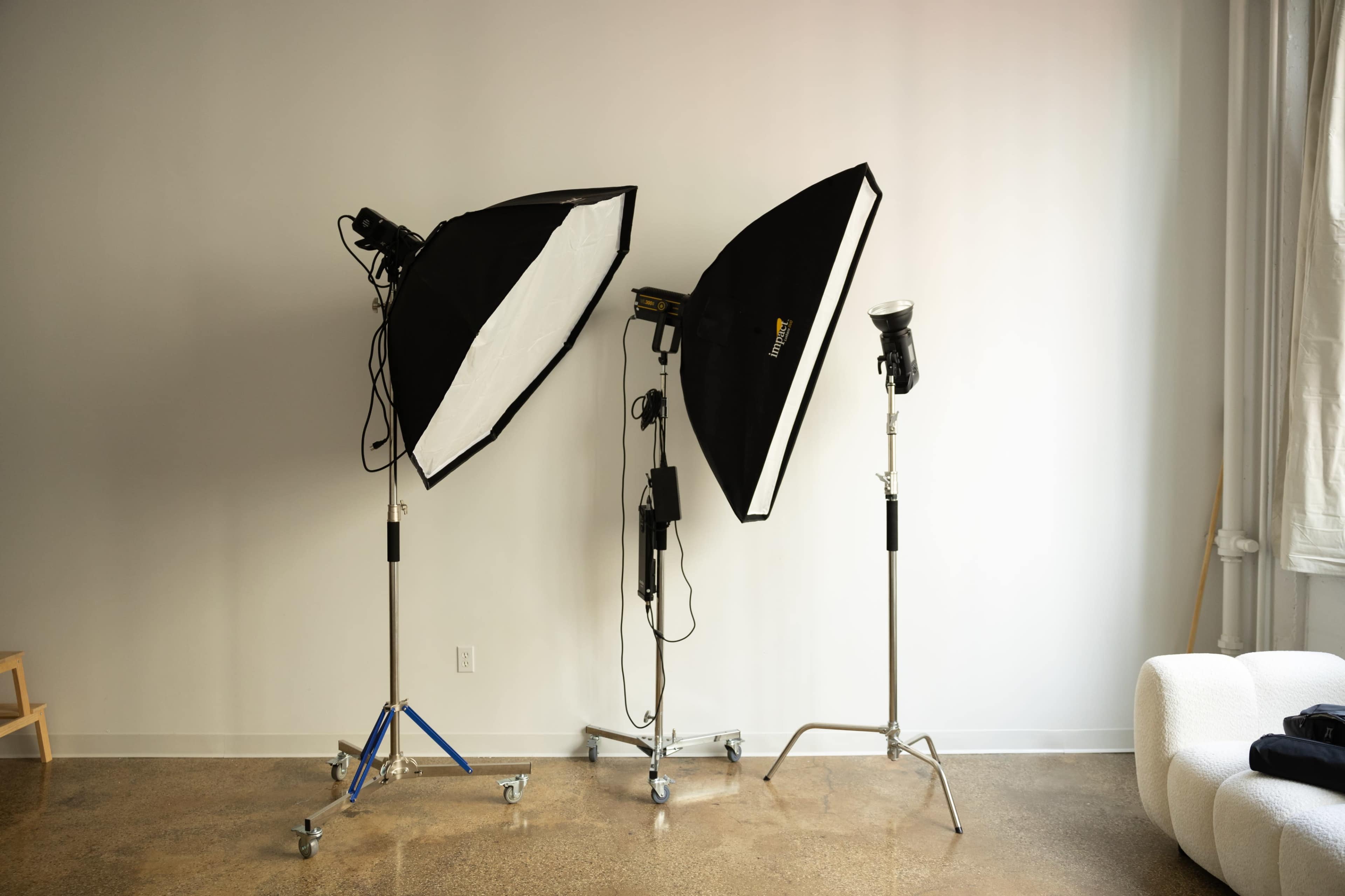 The image shows two studio light setups positioned on stands in a minimalist room with a light-colored wall.