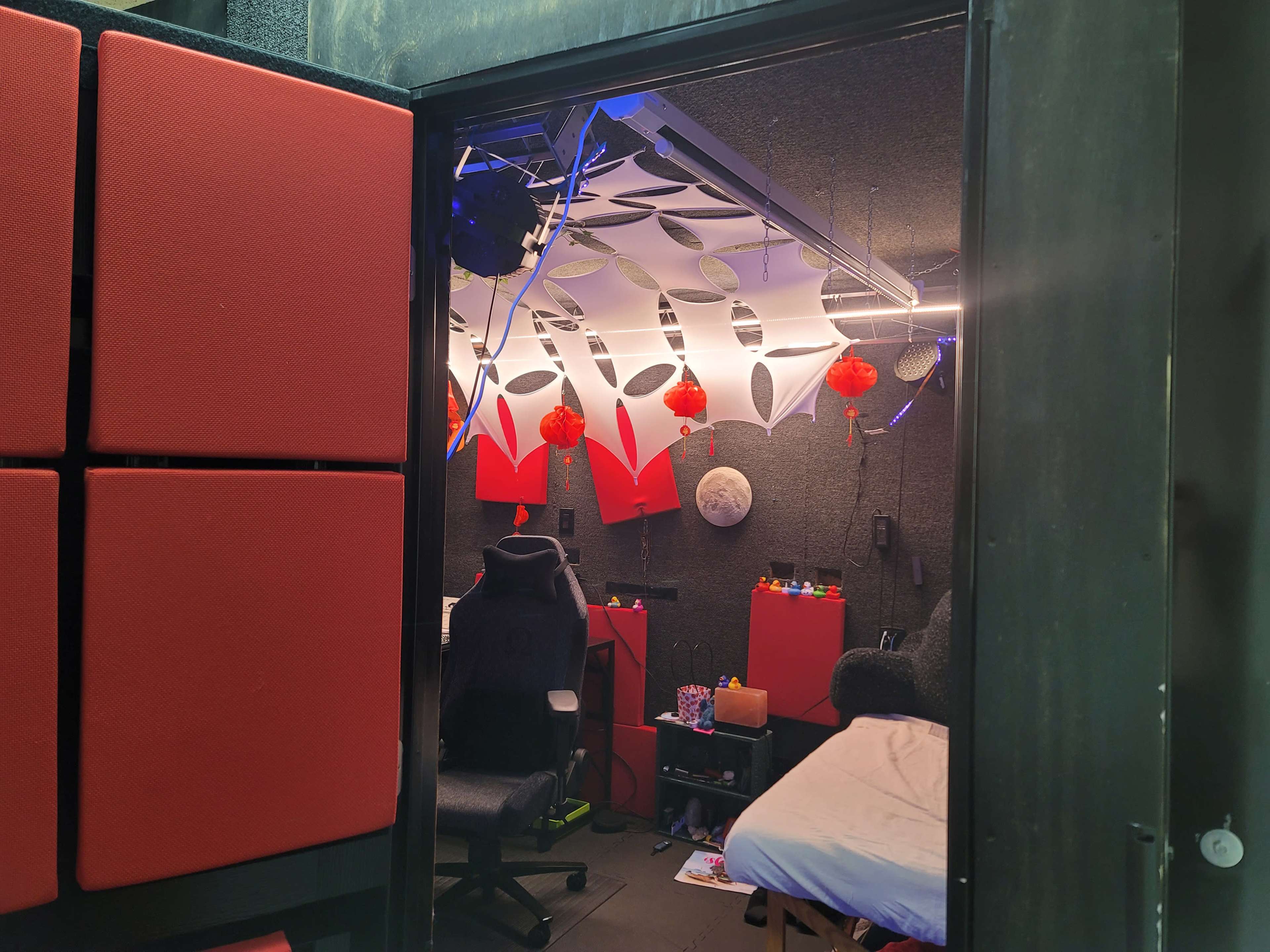 A small room with red acoustic panels, a gaming chair, and decorative lanterns hanging from the ceiling.