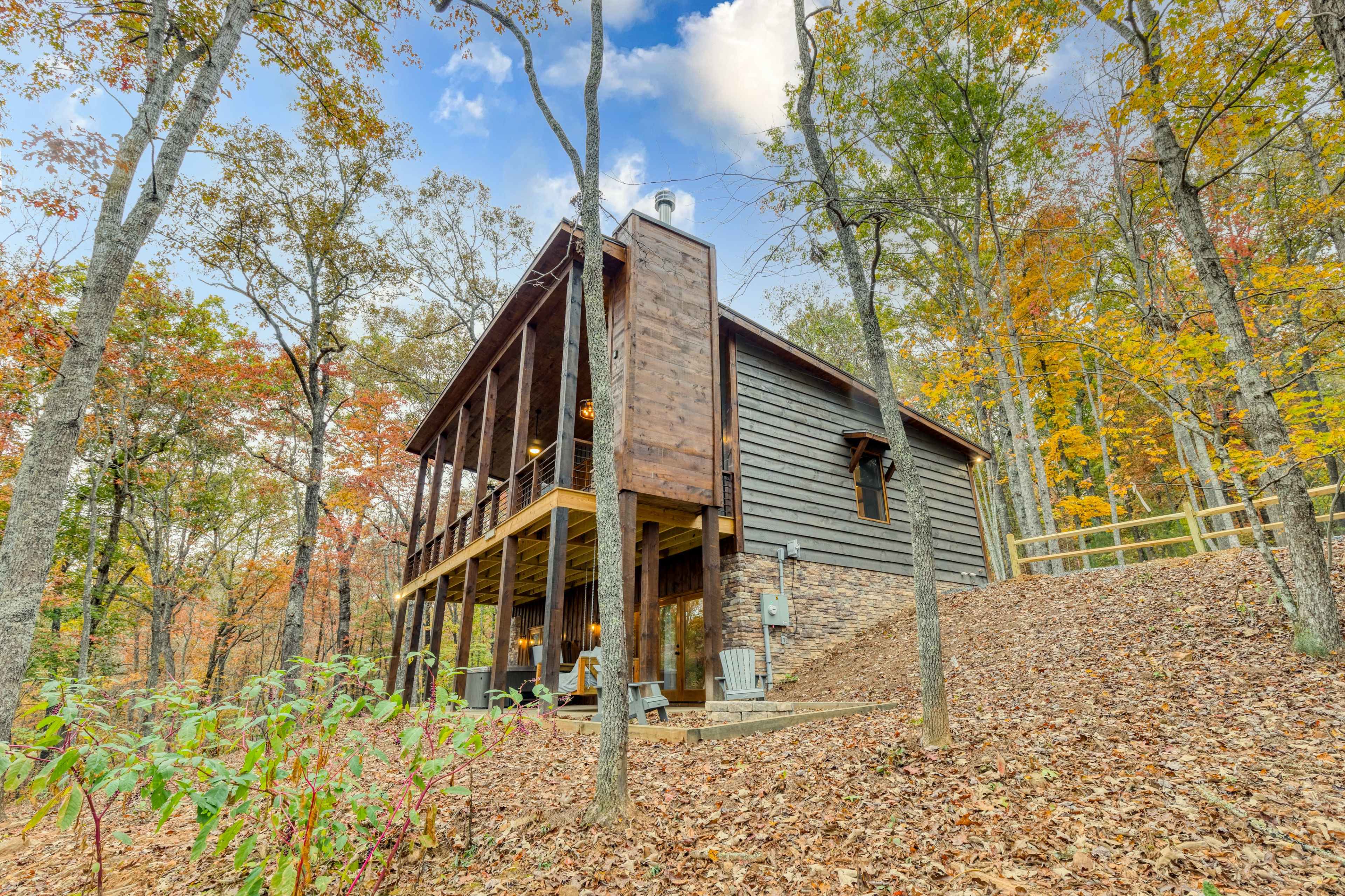 A modern cabin with a wooden exterior is surrounded by trees and colorful autumn foliage.