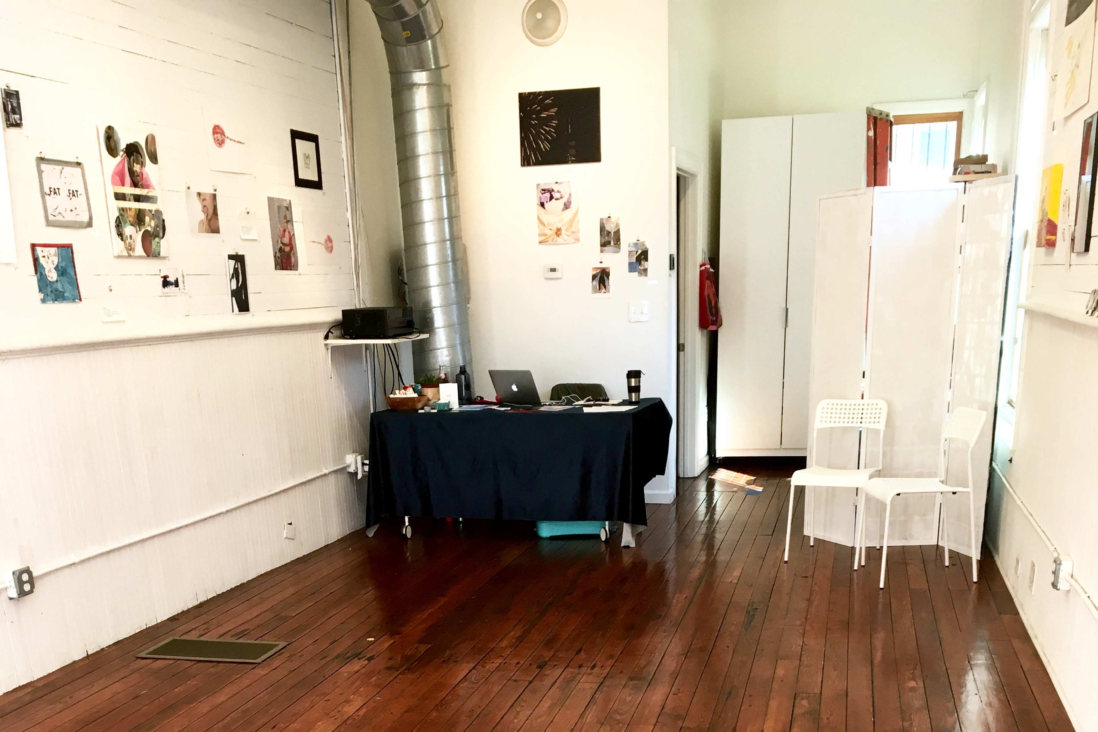 A sparsely furnished room with a table and two white chairs, featuring wooden floors and various decorations on the walls.