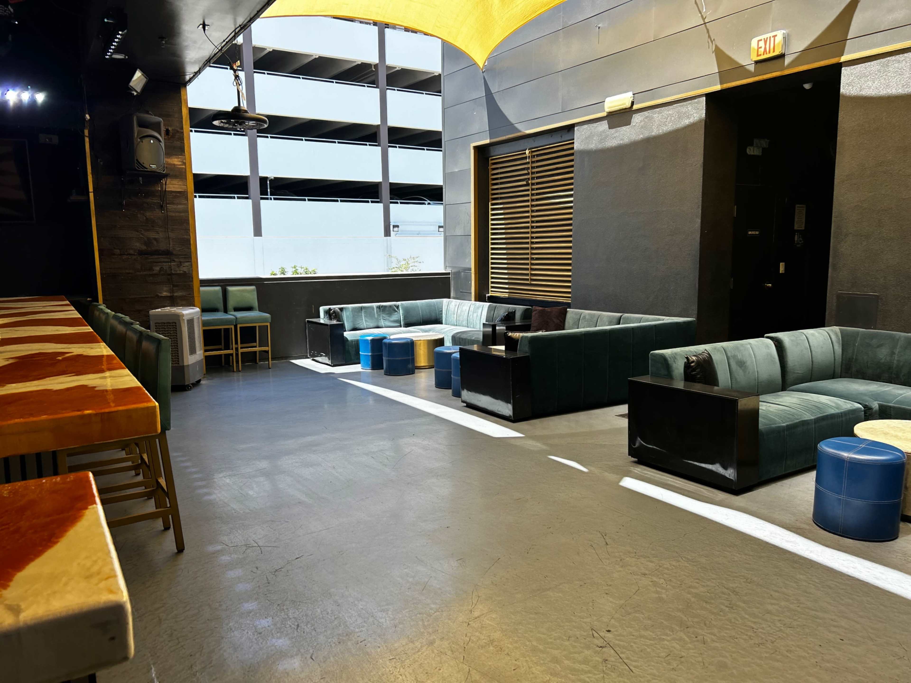 The image shows a modern lounge area with green sofas, round stools, and a long table, illuminated by natural light from large windows.