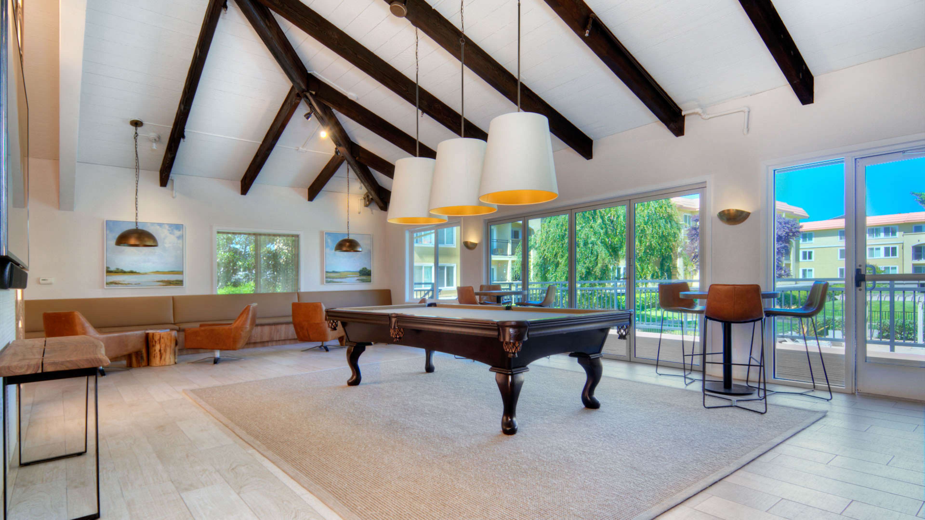 A spacious room features high vaulted ceilings, a billiard table, and large windows overlooking an outdoor area.