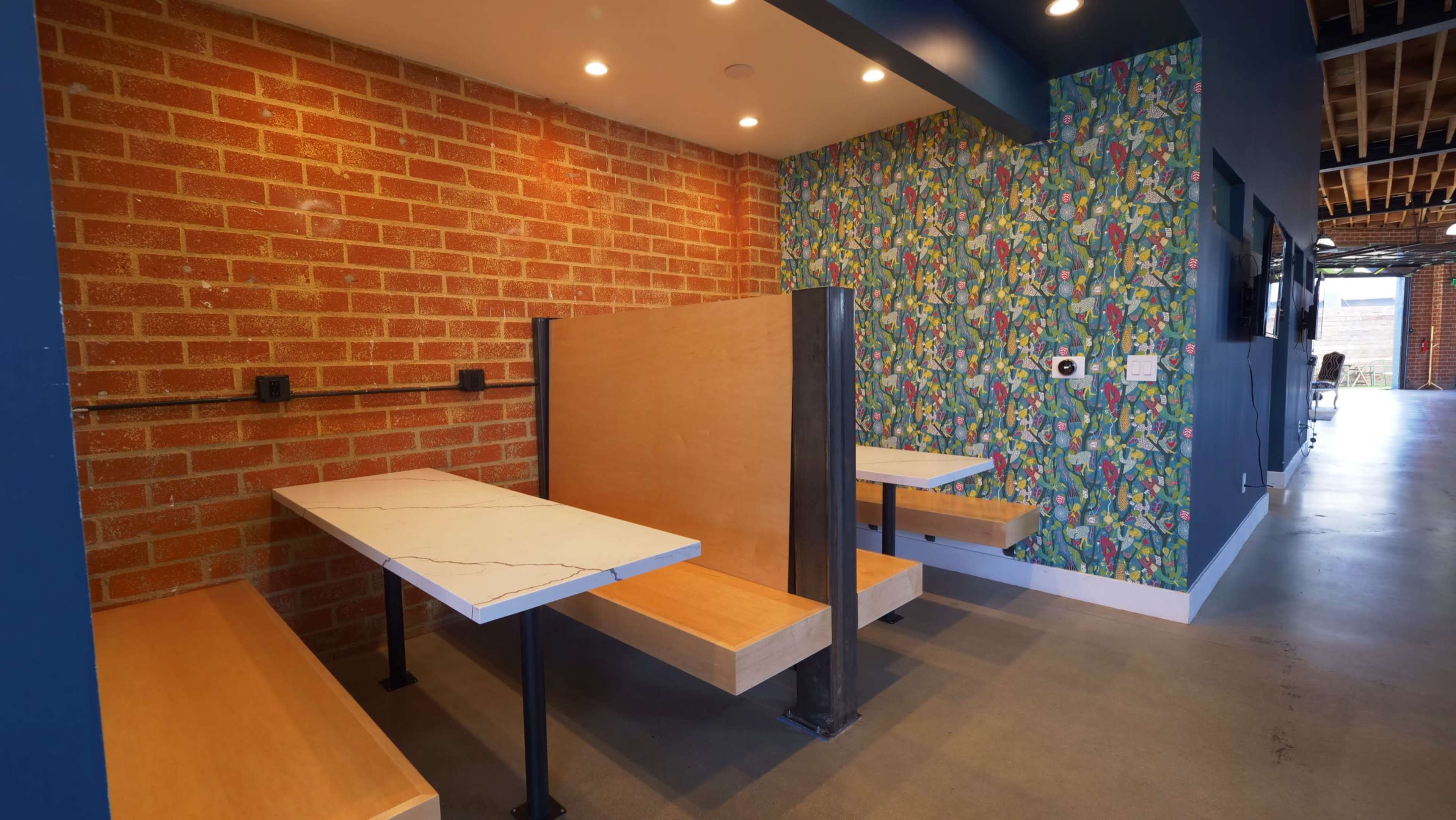 The image shows a modern seating area featuring two booth-style tables against a brick wall and a colorful patterned wall.