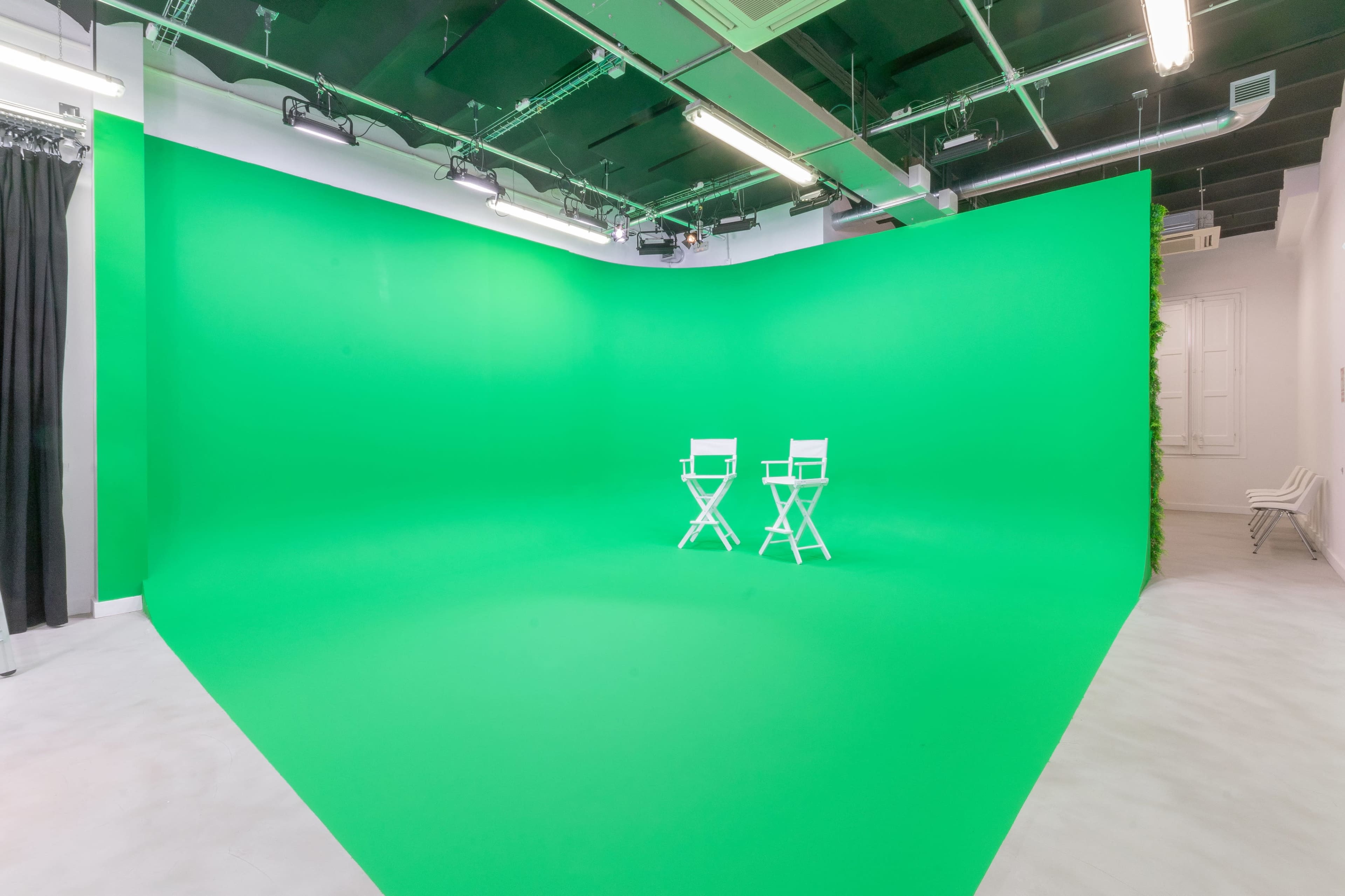 A studio with a bright green backdrop and two white director's chairs positioned in front of it.