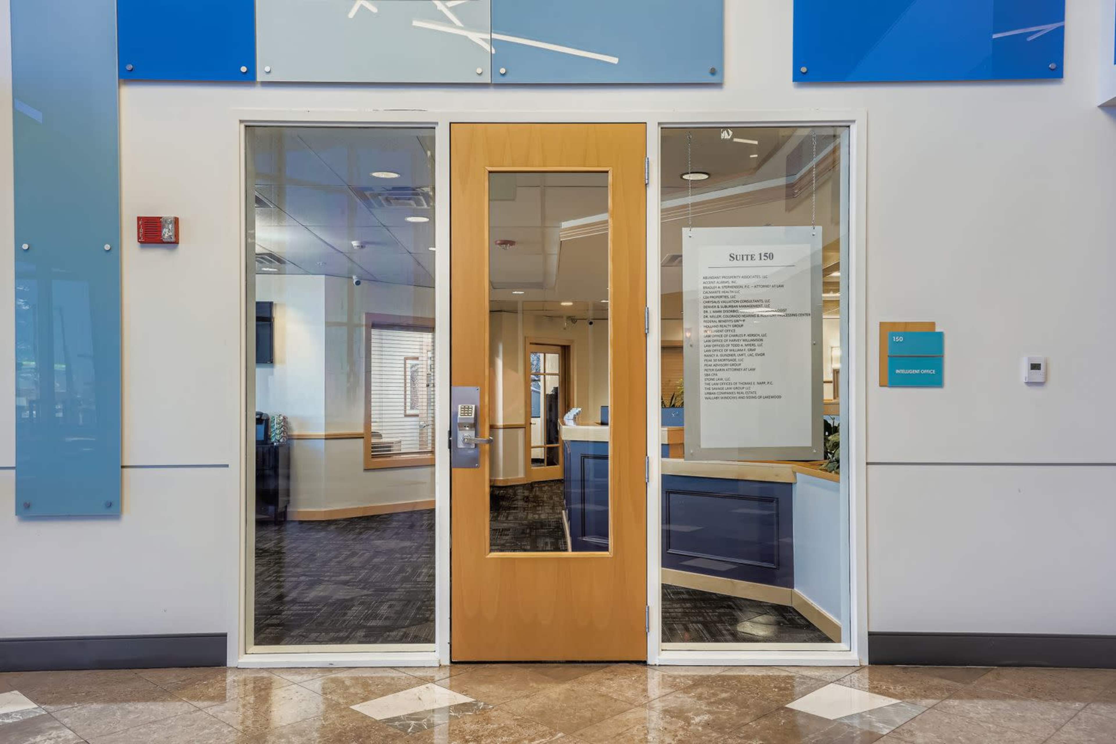 The image shows a glass door with a wooden frame leading into an office space, featuring a sign on the left side that provides information about the suite.