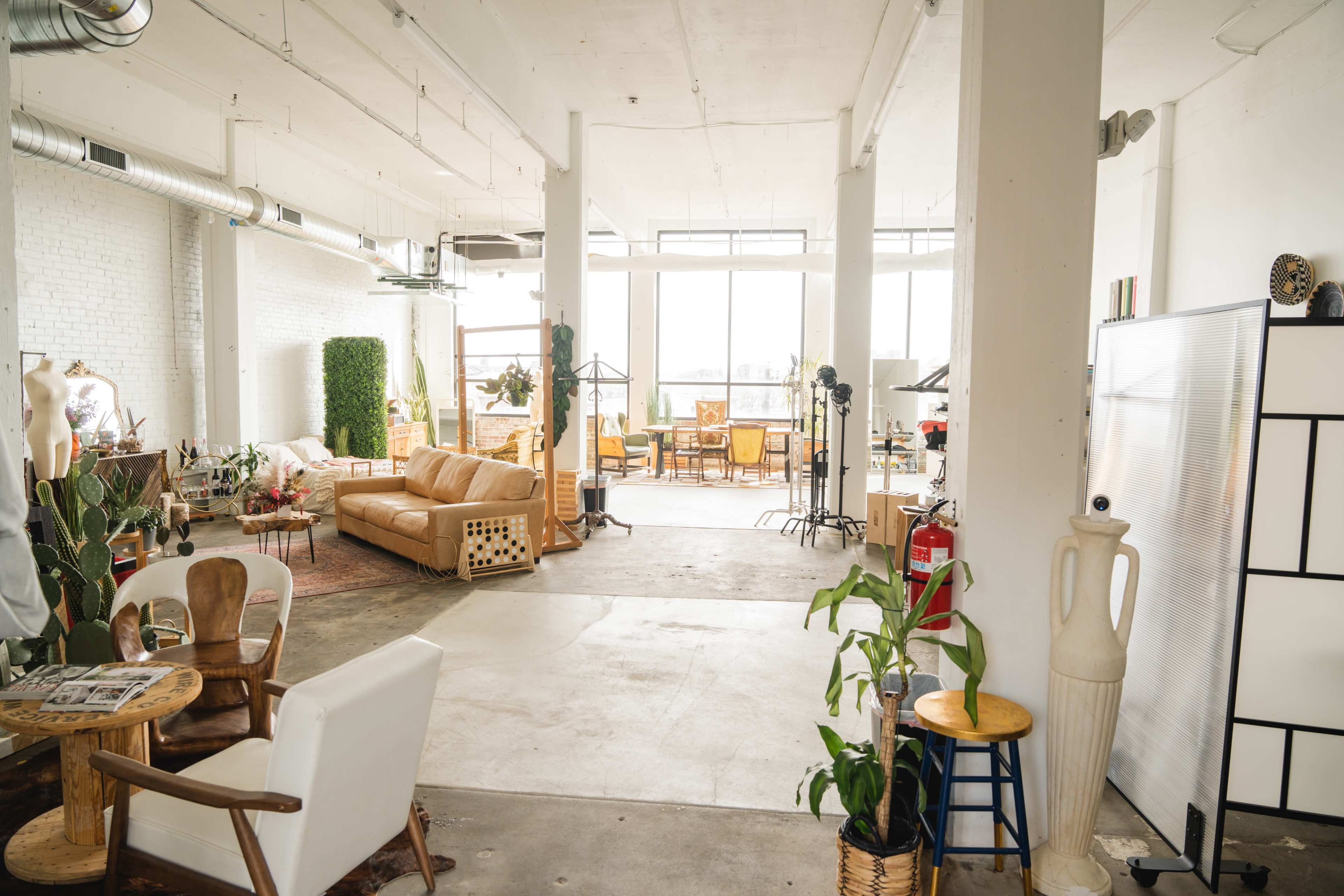 A spacious, well-lit studio with various pieces of furniture and décor, including a sofa, chairs, and plants.