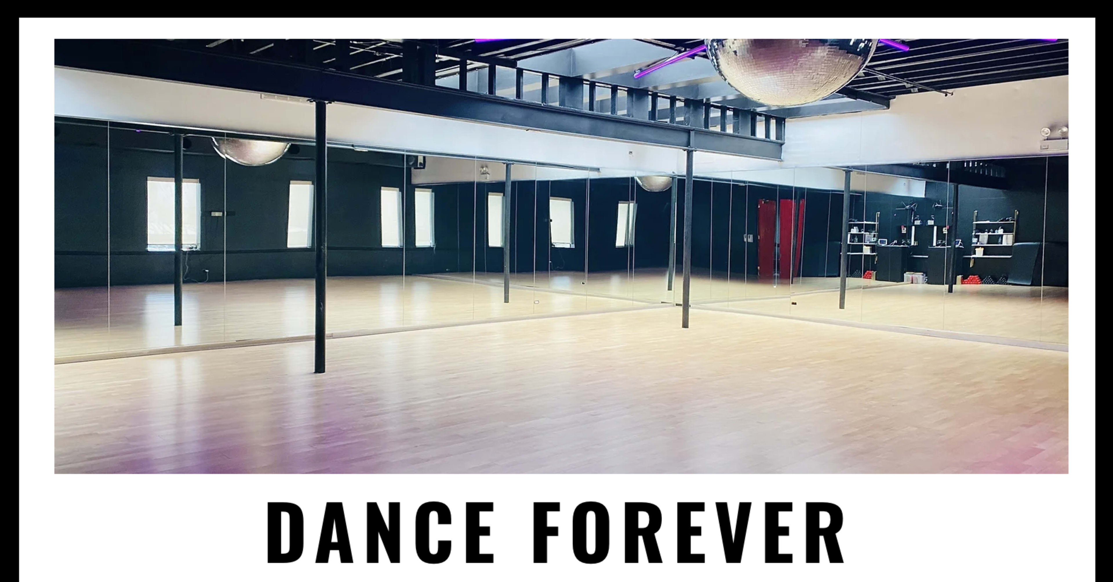 A spacious dance studio features wooden flooring, large mirrors on one wall, and a disco ball hanging from the ceiling.
