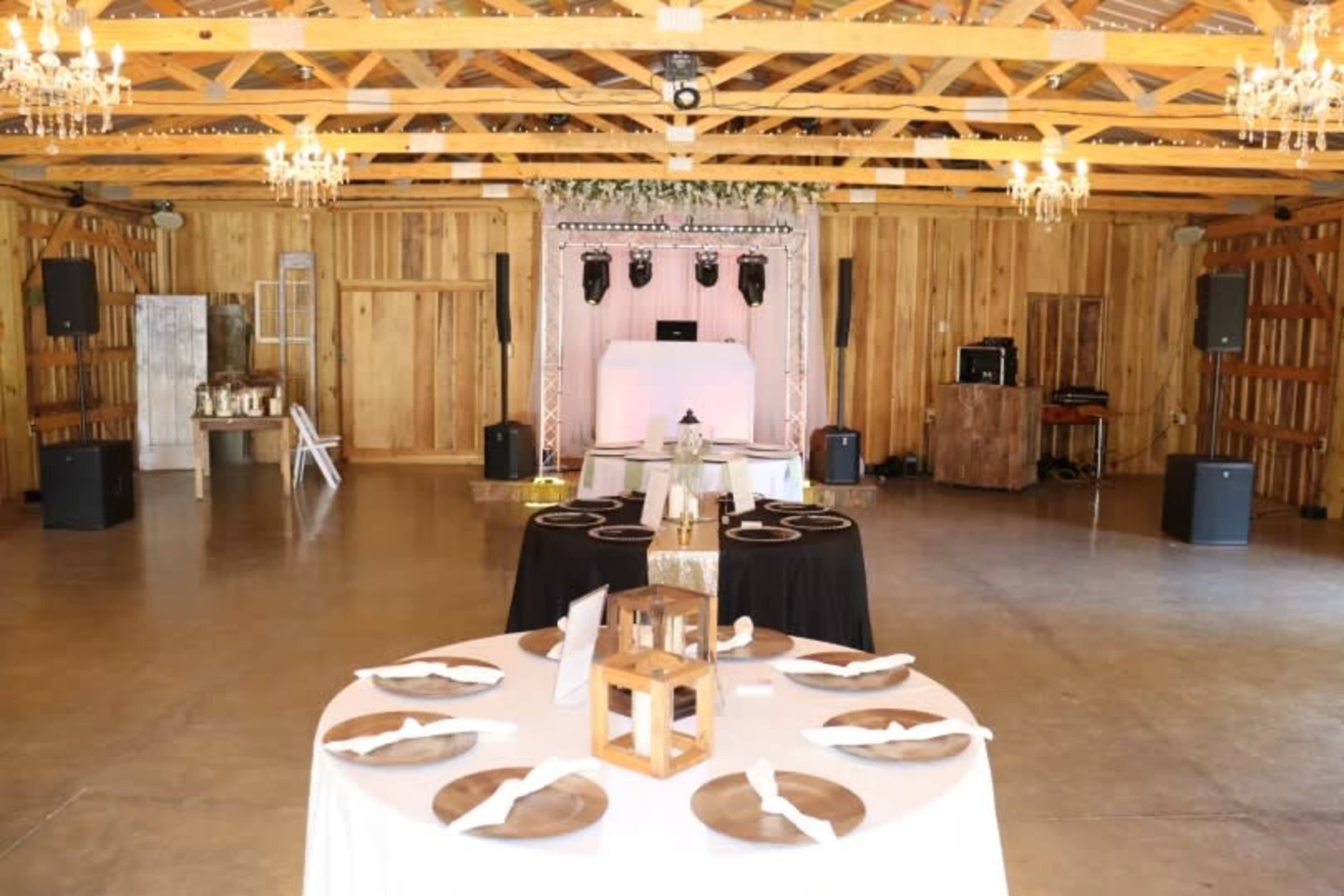 A spacious event venue with wooden walls, tables set for dining, and a stage area equipped with sound equipment and decorative elements.