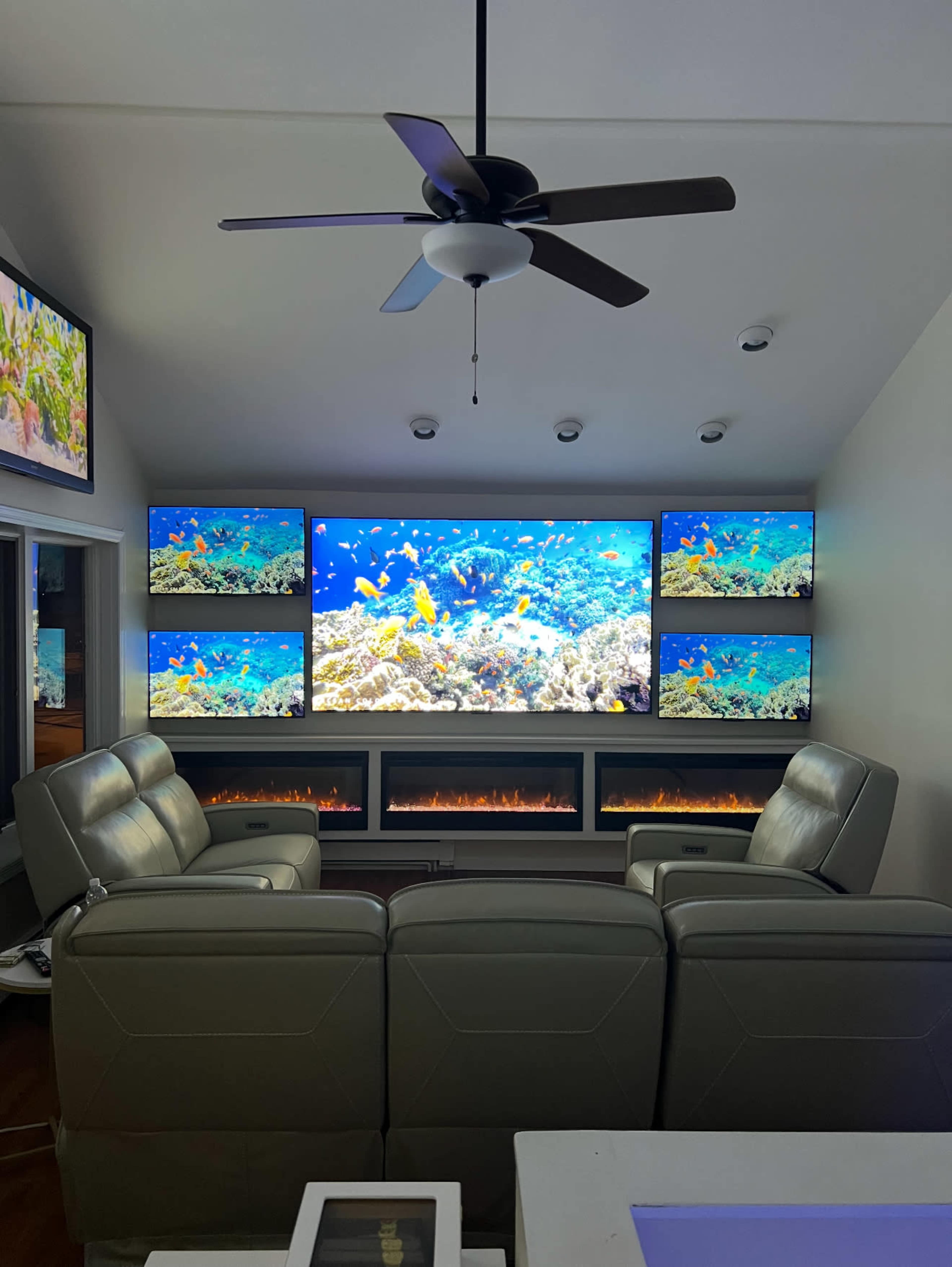 A living room features multiple large screens displaying an underwater scene, flanked by a modern seating area and an electric fireplace below.