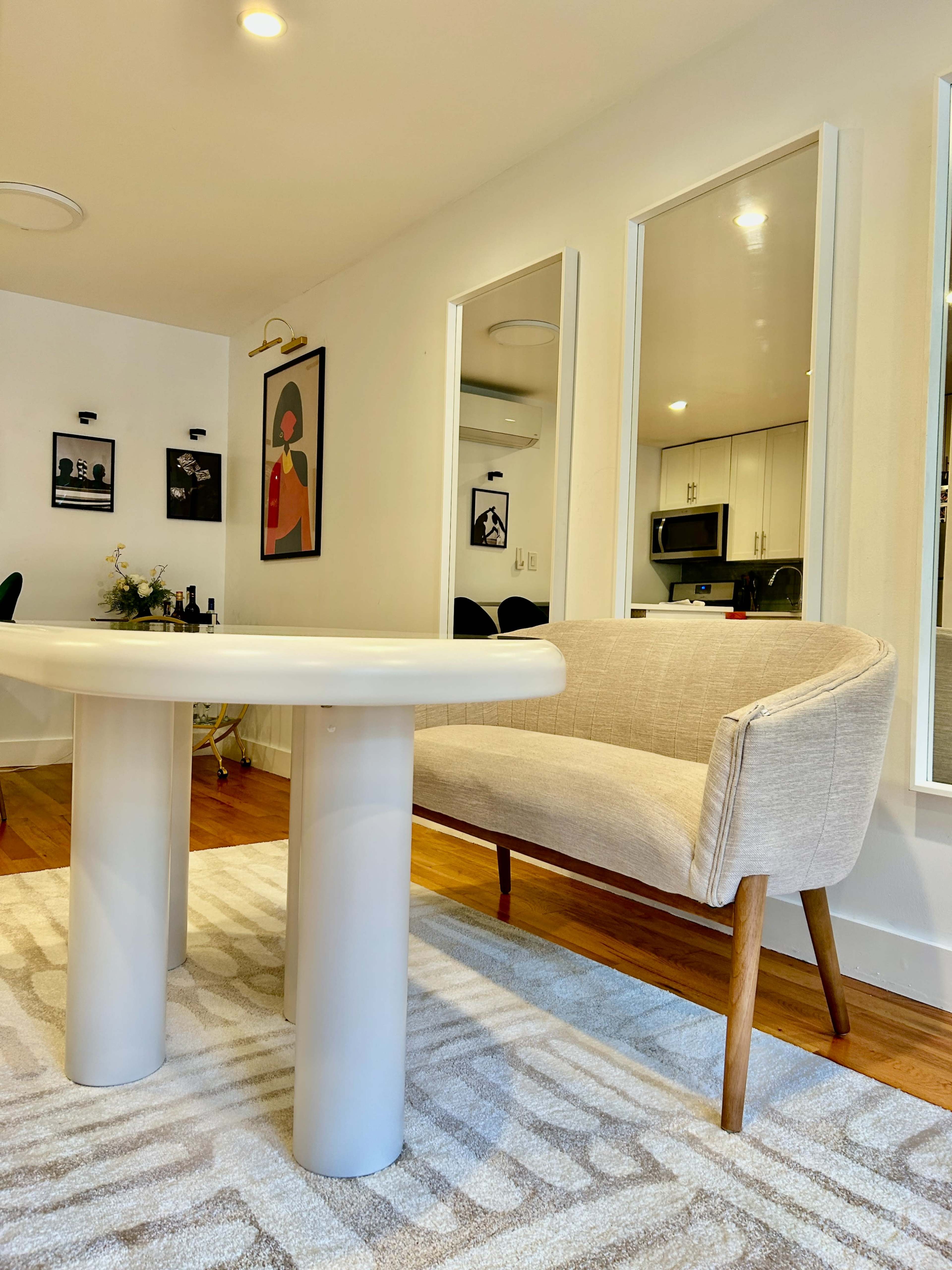 A round white table is set near a beige armchair in a bright room with mirrors and framed artwork on the walls.