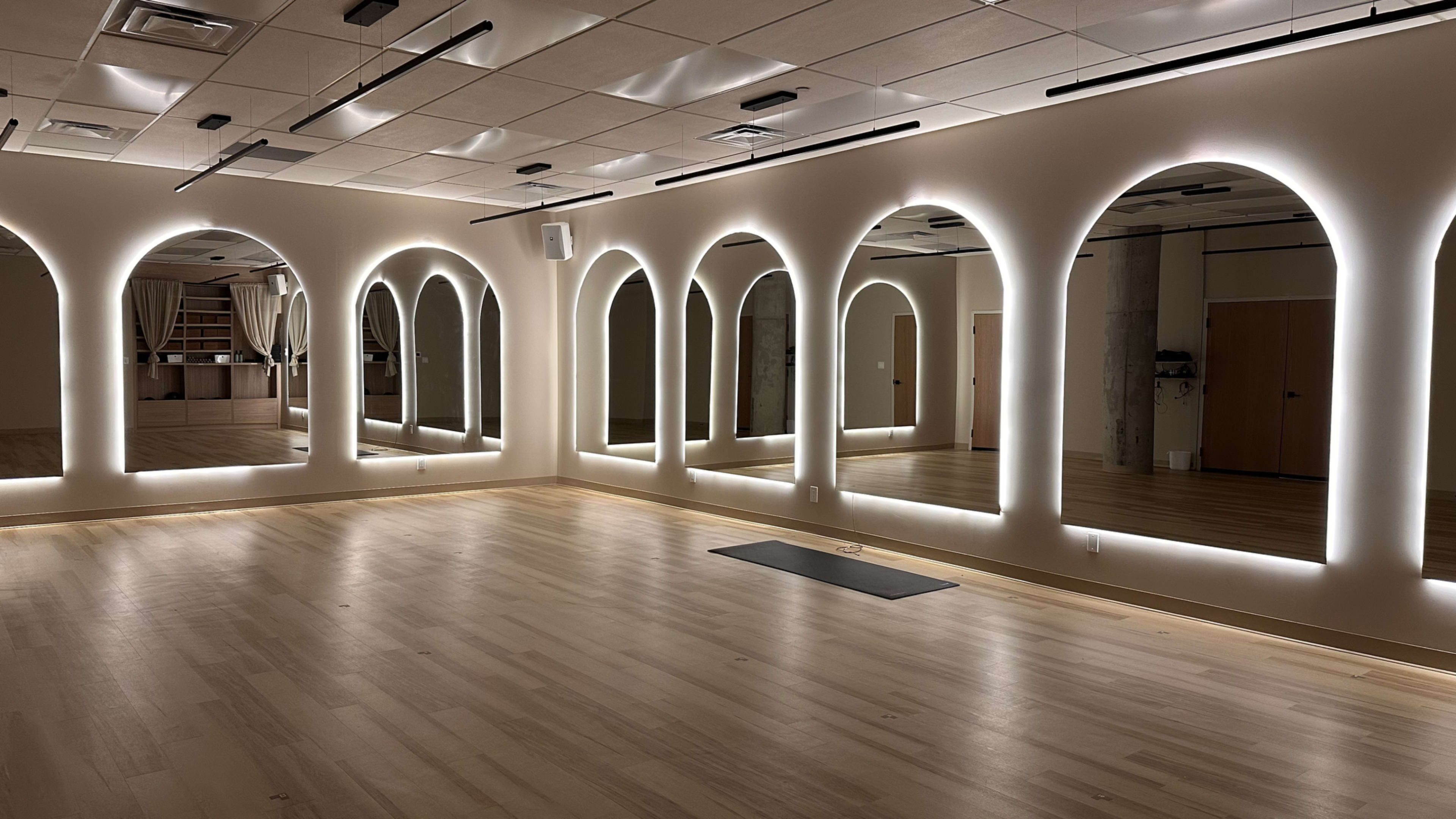 The image shows a spacious room with wooden flooring and several large, illuminated arch-shaped mirrors along the walls.