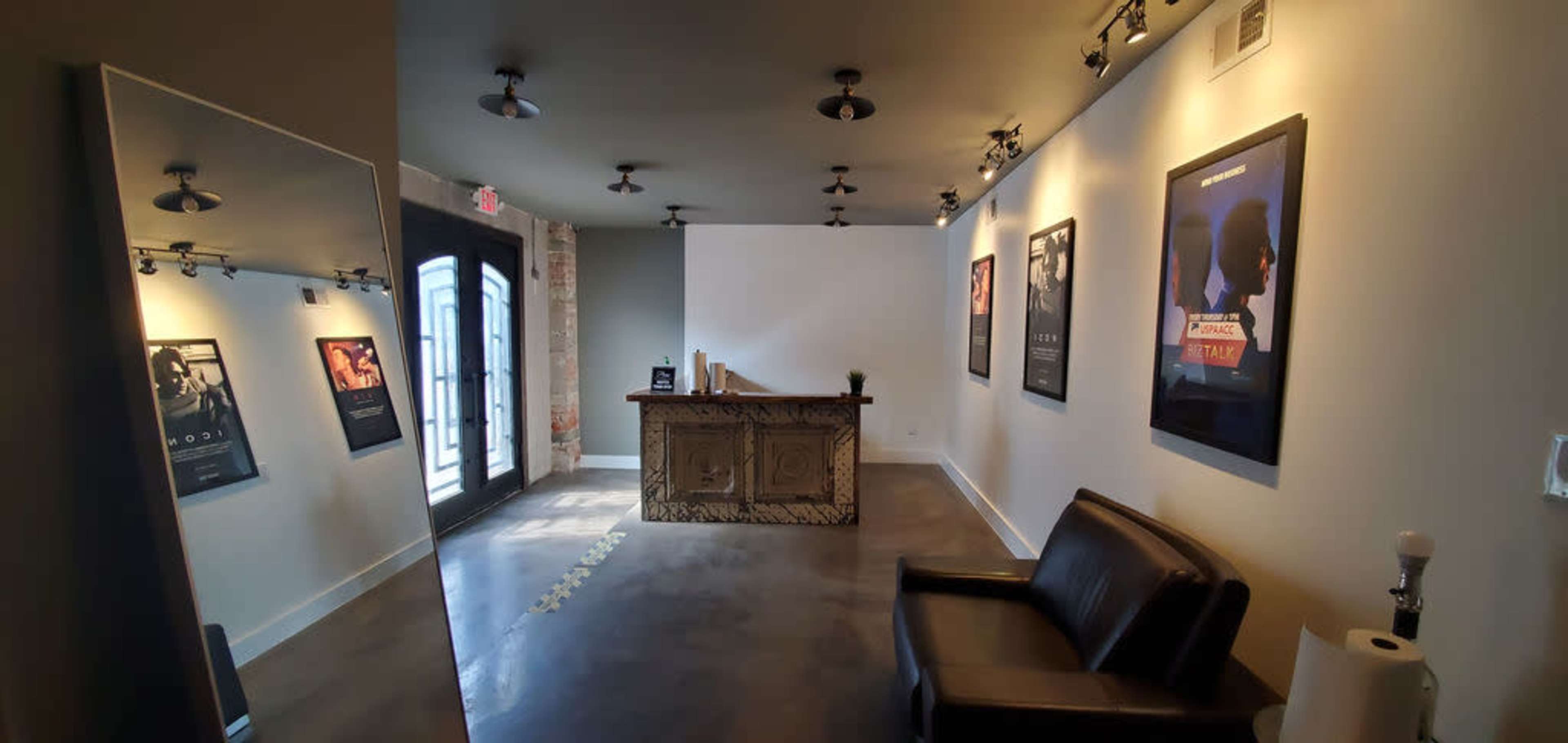 A modern reception area featuring a wooden front desk, a black leather chair, and movie posters on the walls, with a large mirror reflecting the space.