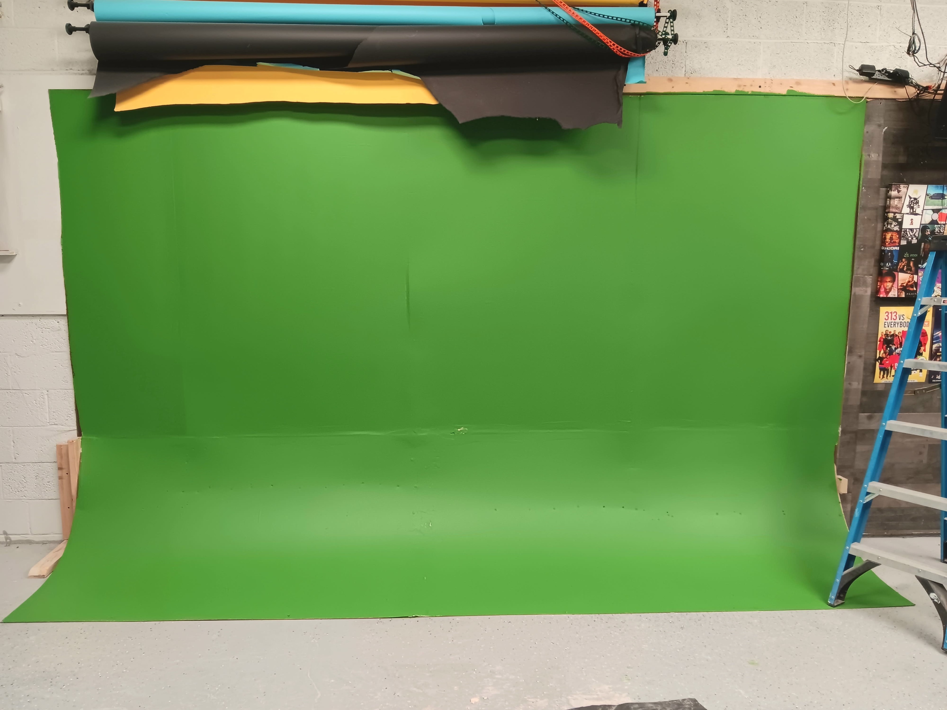The image shows a green screen setup with various colored backdrops and a ladder in a studio environment.