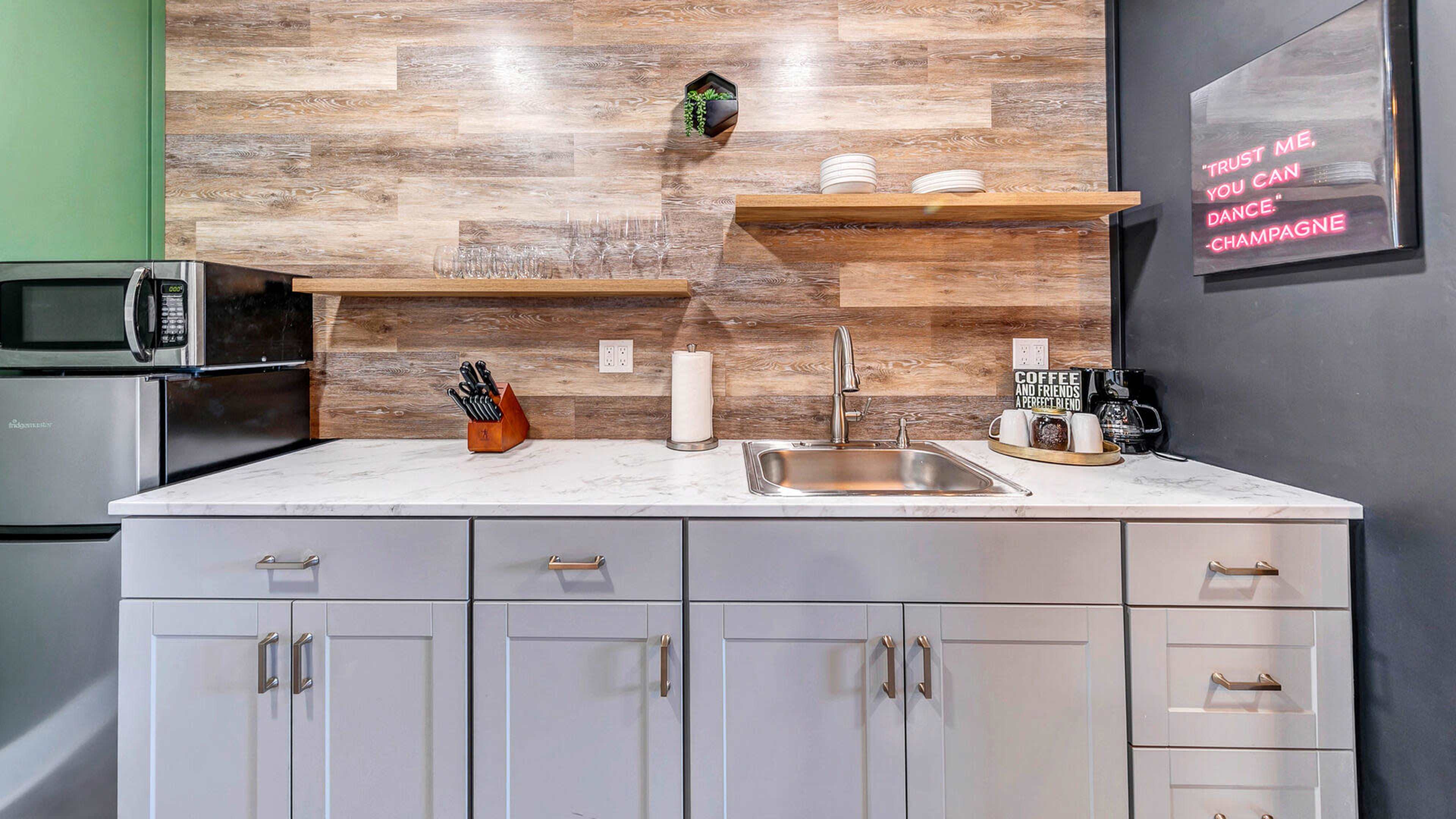 A modern kitchen with wood-panelled walls, a marble countertop, and open shelving displaying dishes and kitchen tools.