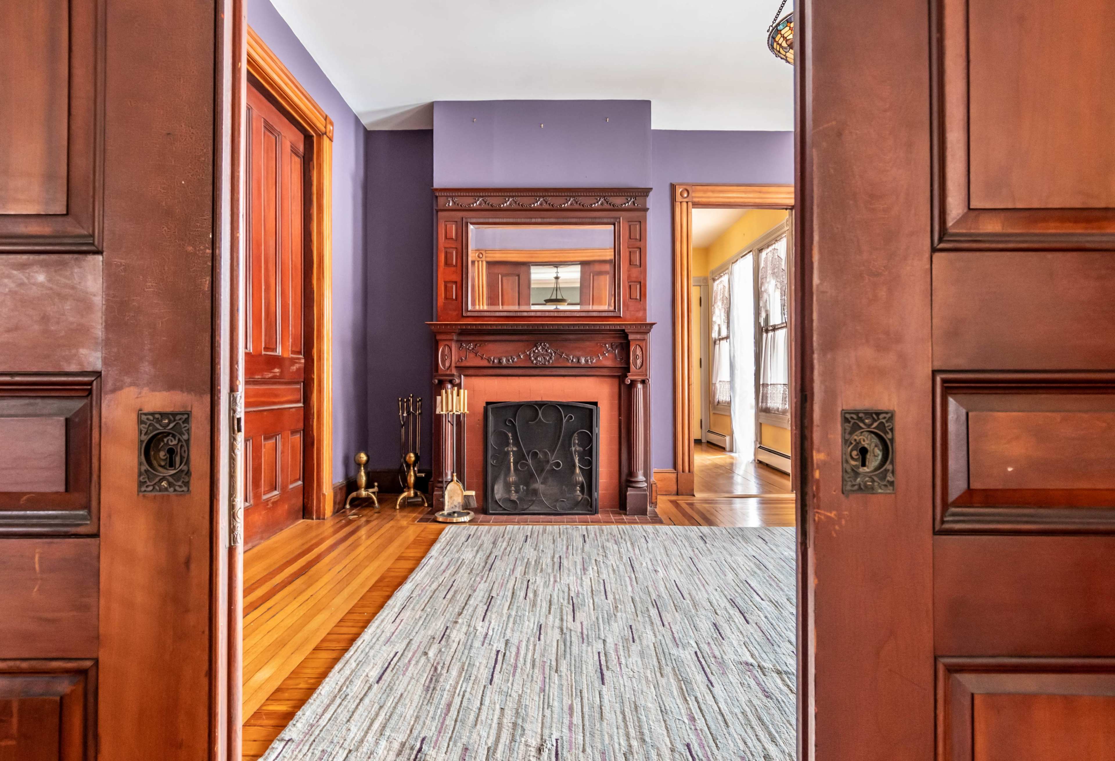 A view through open wooden doors reveals a room with a fireplace and a patterned rug on a wooden floor.