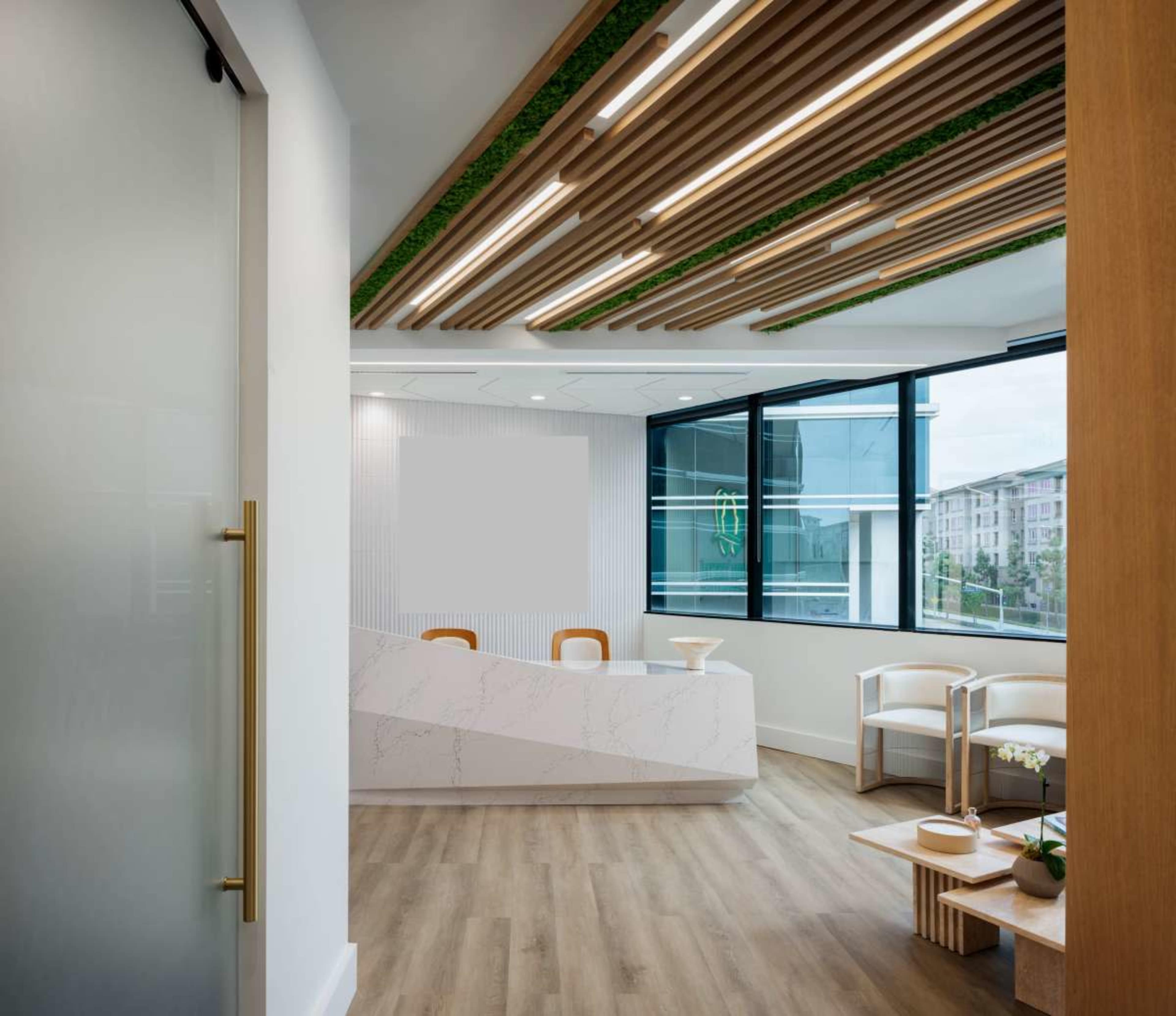 The image shows a modern reception area with a minimalist design featuring a curved front desk, seating, and large windows allowing natural light to enter.