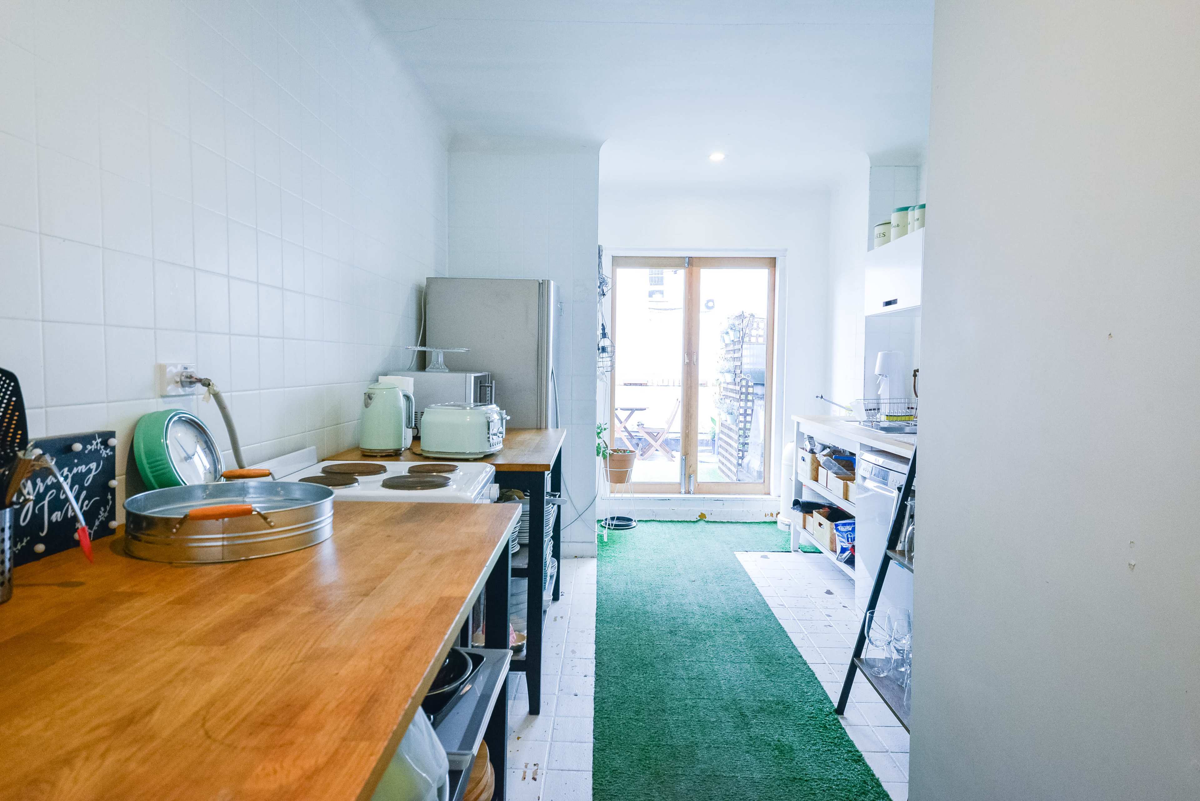 A narrow kitchen with wooden countertops, a refrigerator, and a door leading to an outdoor balcony.