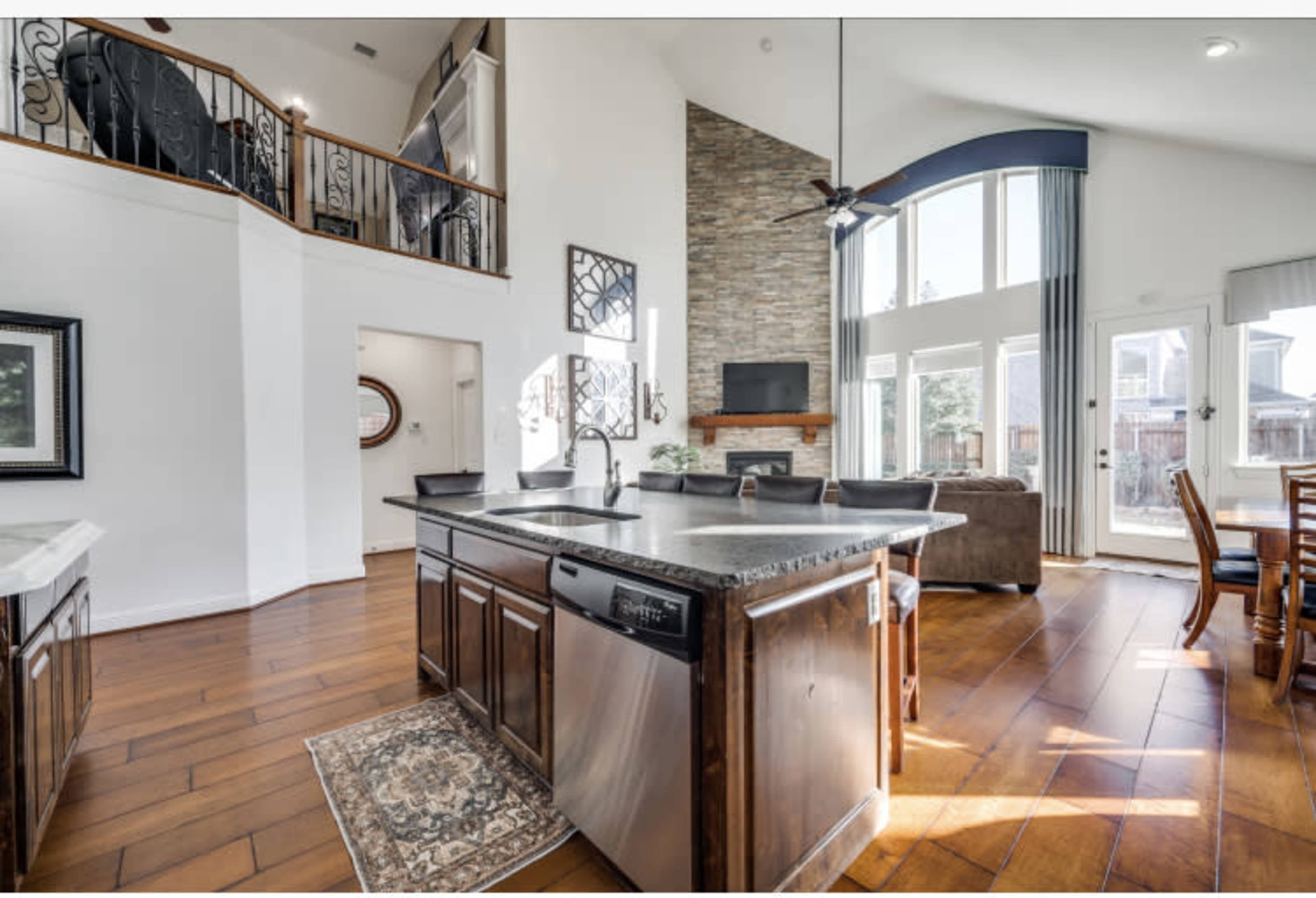 The image shows a spacious open-concept kitchen and living area with a large island, wooden flooring, and a stone fireplace.